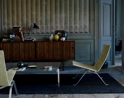 PK22 Sessel von Fritz Hansen in beigem Leder und Stahlgestell vor dunkler Wand.