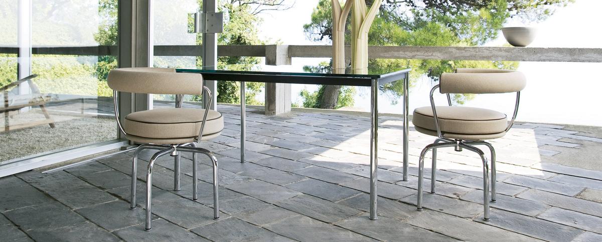 Zwei Cassina Drehsessel "7 Fauteuil Tournant" mit beigen Polstern und Chromgestell an einem Tisch.