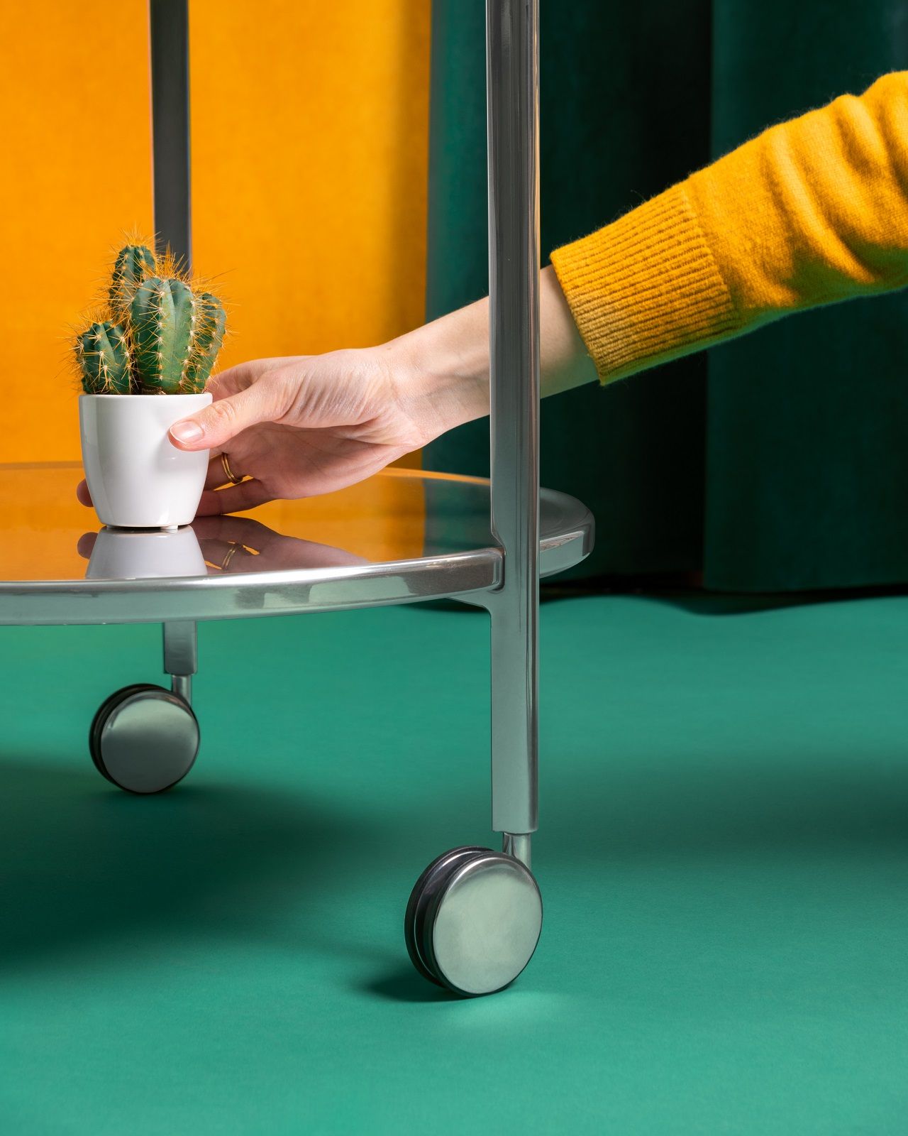 Tambour Beistelltisch von Magis: Hand stellt Kaktus auf silbernen, modernen Rollwagen mit Glasplatte.