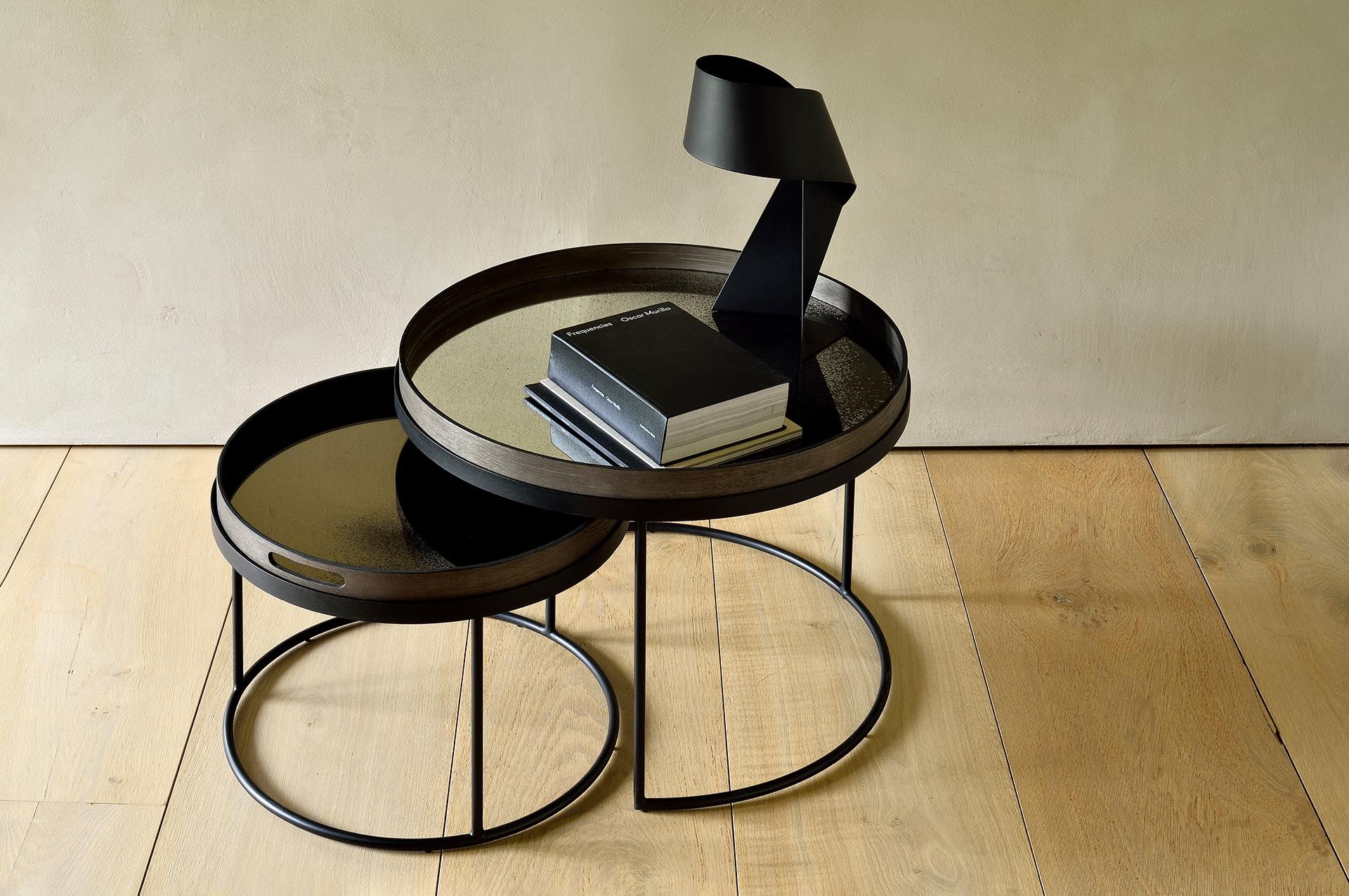 Ethnicraft Couchtisch 2er Set, rund, schwarz mit Spiegelplatte und Buch auf dem oberen Tisch.