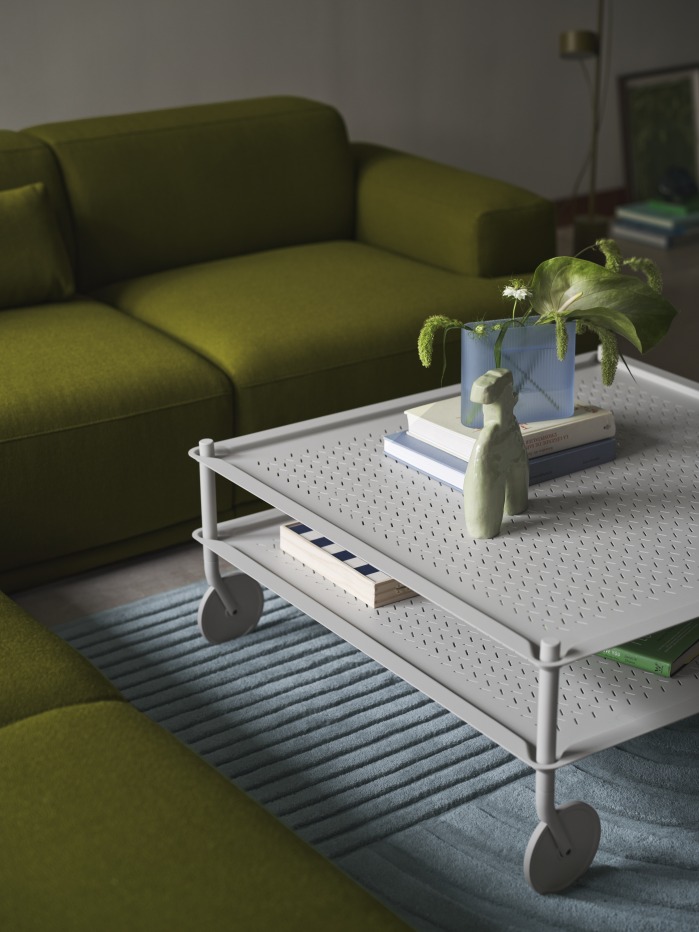 Grauer Flow Coffee Table Couchtisch auf Rollen, mit Deko, vor grünem Sofa.