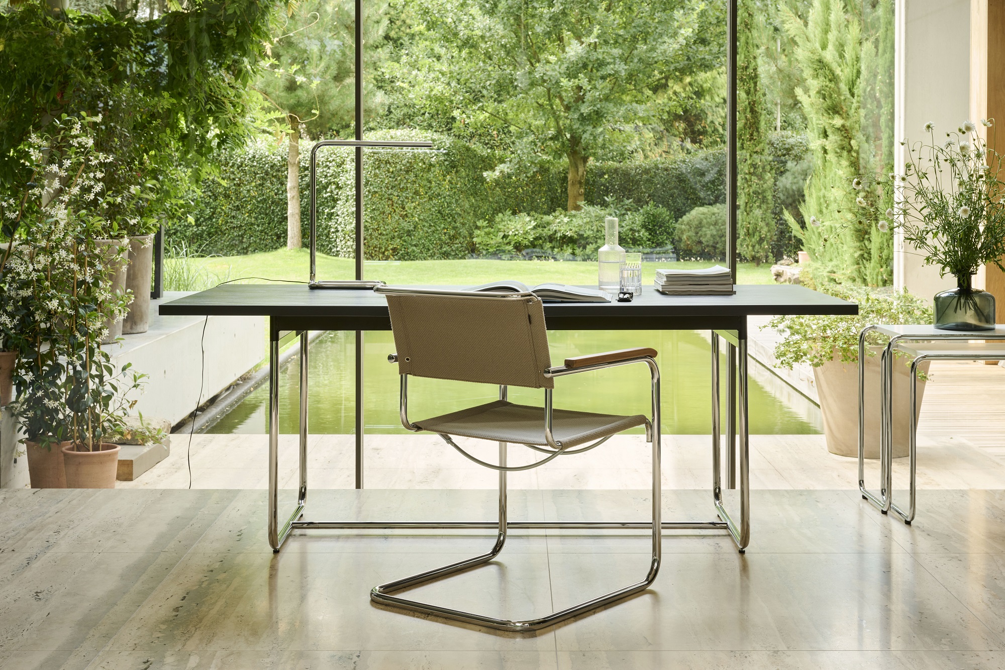 Thonet S 34 Freischwinger Stuhl mit Stoffbezug und Holzarmlehnen am Schreibtisch vor Fenster mit Gartenblick.