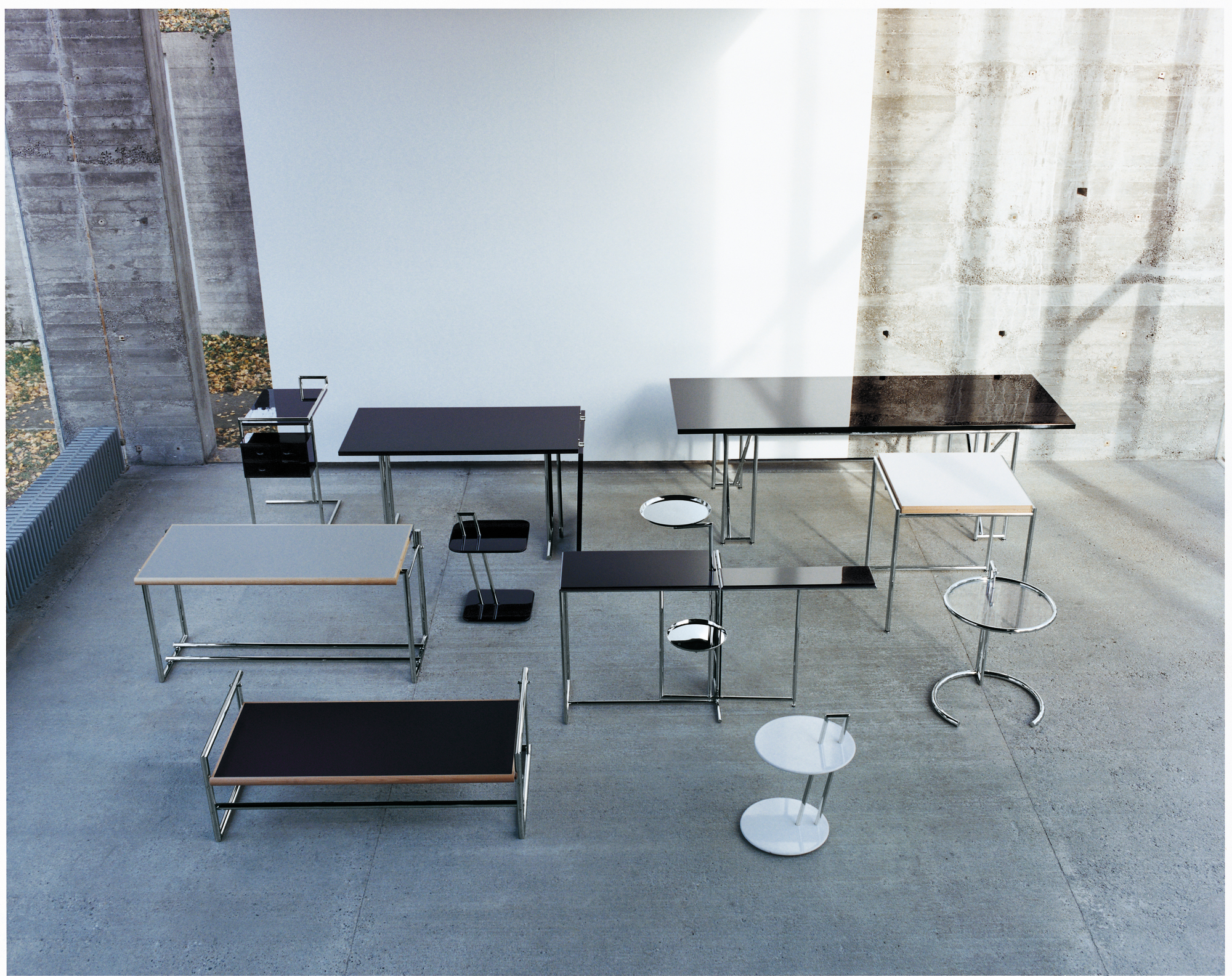 Verschiedene ClassiCon Beistelltische, darunter der Adjustable Table E1027, aus unterschiedlichen Perspektiven in einem Raum.