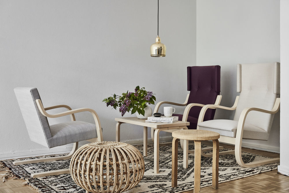 Wohnzimmer-Szene mit Artek A330S Golden Bell Pendelleuchte über einem Tisch, umgeben von Stühlen und Dekoration.