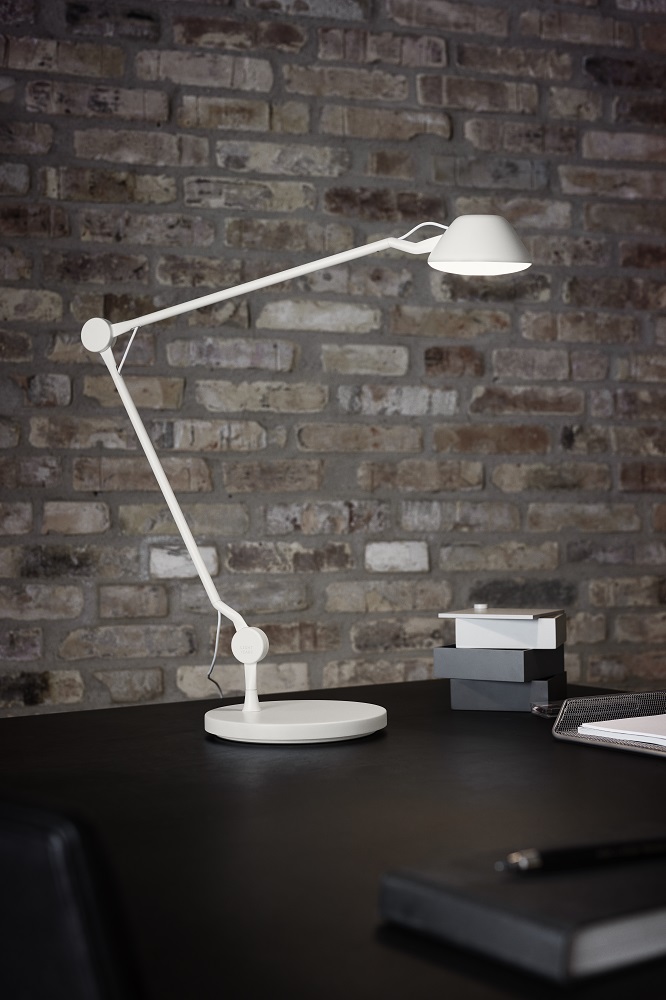 Weiße AQ01 Tischleuchte von Fritz Hansen auf einem Schreibtisch vor einer Backsteinwand.