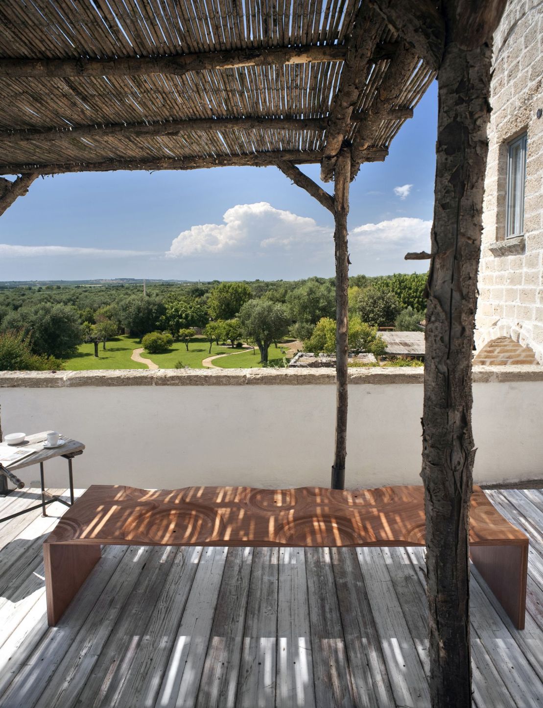 Holzbank für den Außenbereich auf einer Terrasse mit Blick auf eine grüne Landschaft. Designermöbel für Garten und Balkon.