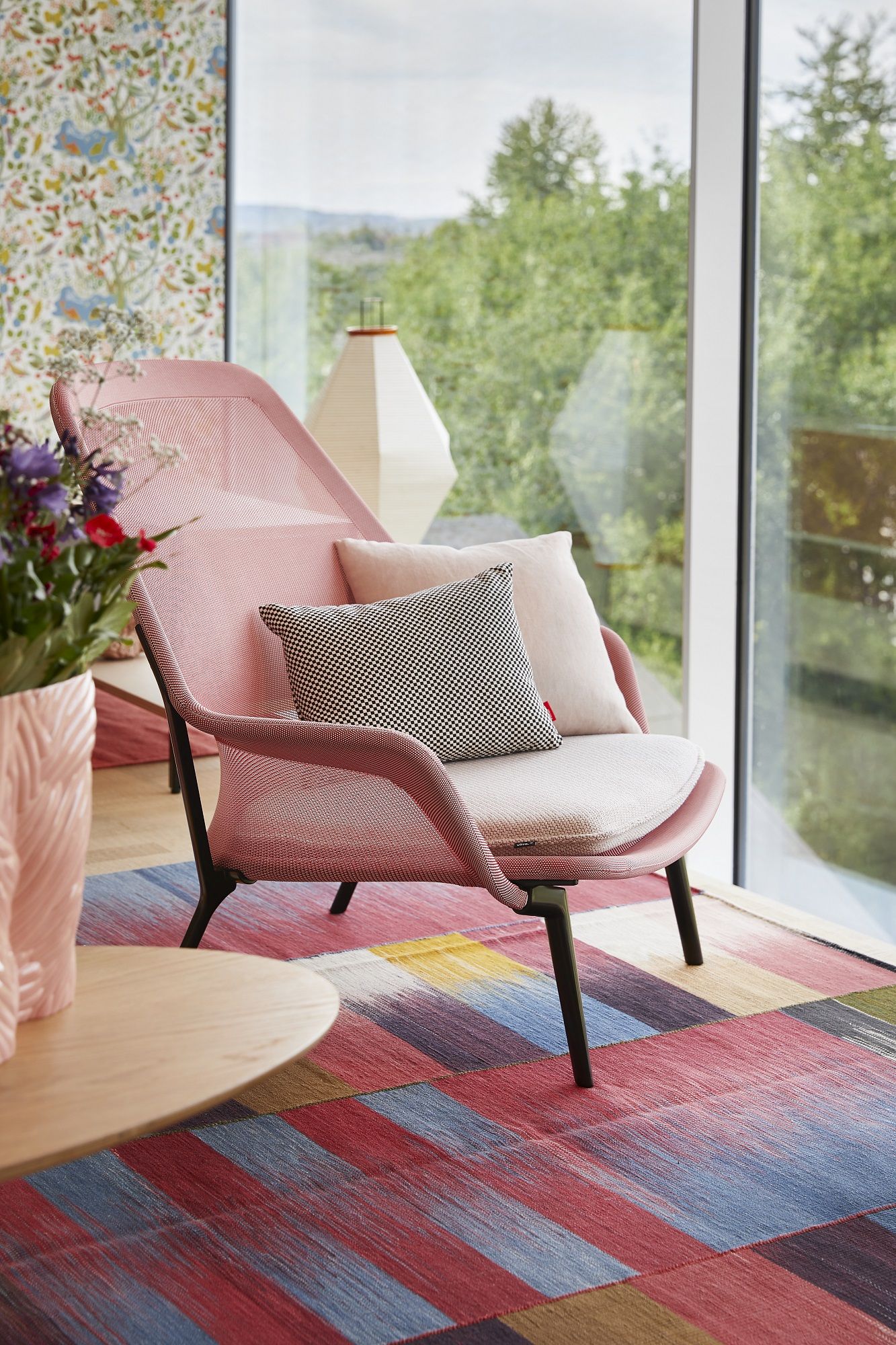 Rosa Vitra Slow Chair Sessel mit Kissen vor Fenster und farbenfrohem Teppich für entspanntes Wohnen.