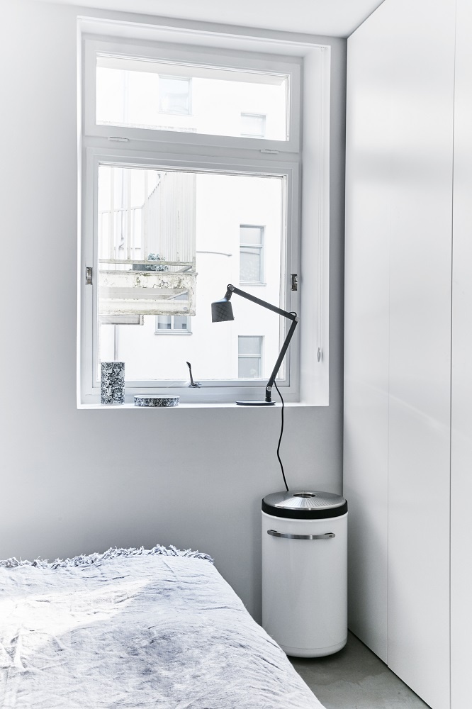 Weißer Vipp Wäschekorb im Schlafzimmer, neben Bett und Fenster mit Lampe.