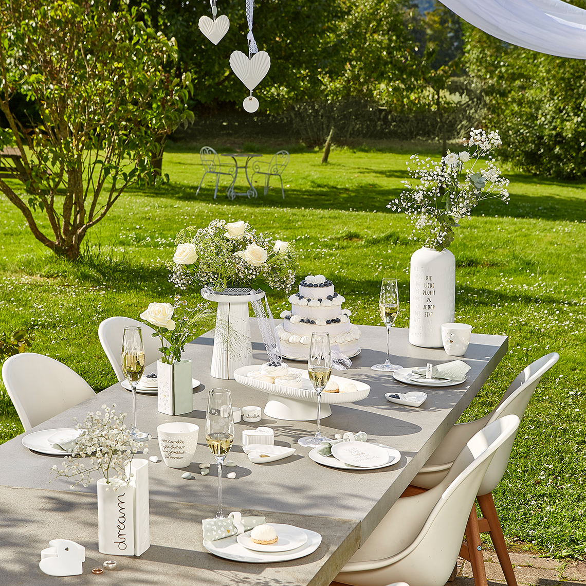 Hochzeitstafel im Garten mit Anrichteplatte, Tortenständer, Blumenschmuck und Champagnergläsern für eine festliche Feier.