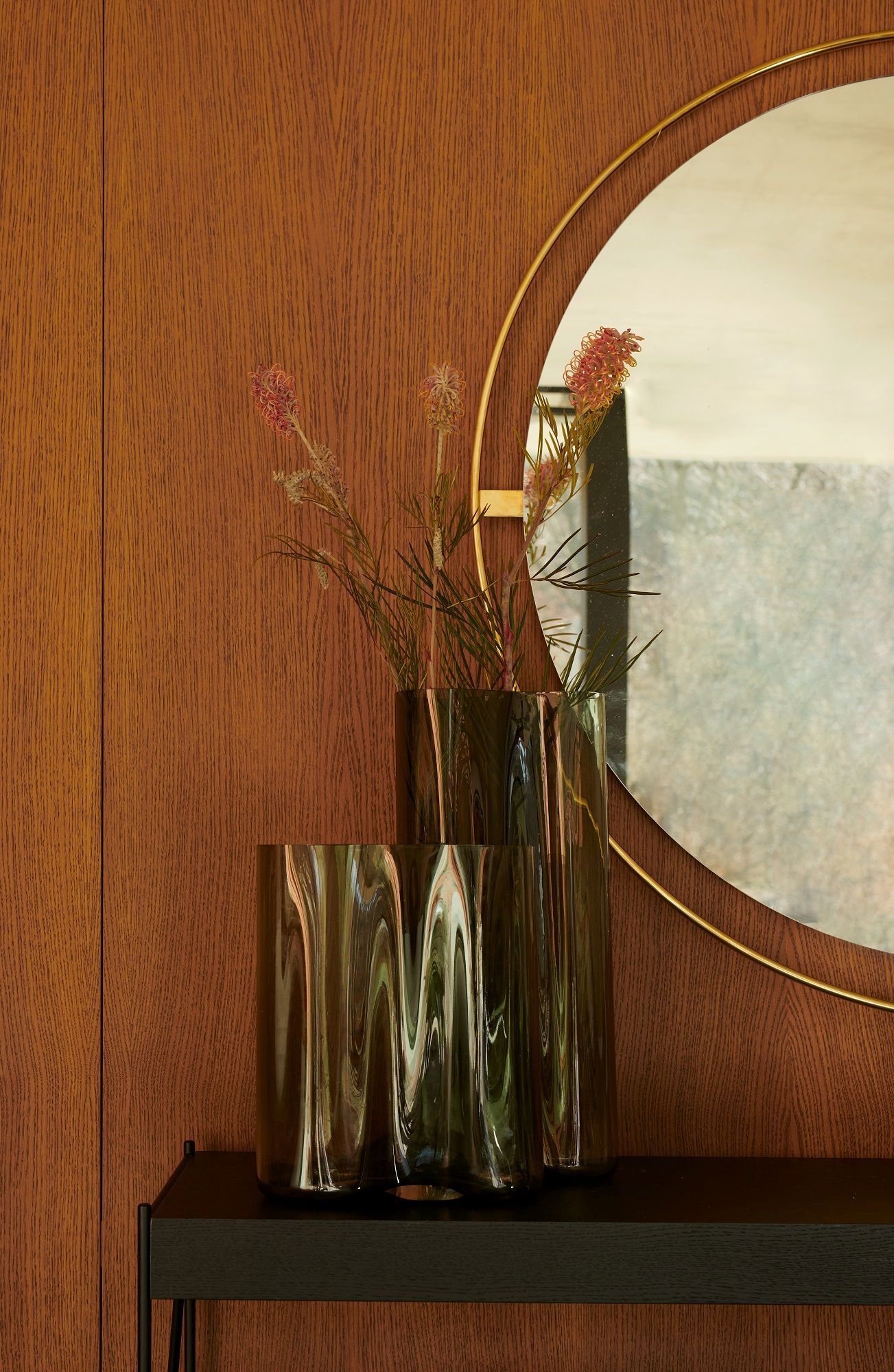 Audo Copenhagen Nimbus Mirror mit Goldrahmen, kombiniert mit dekorativen Vasen und Blumen.