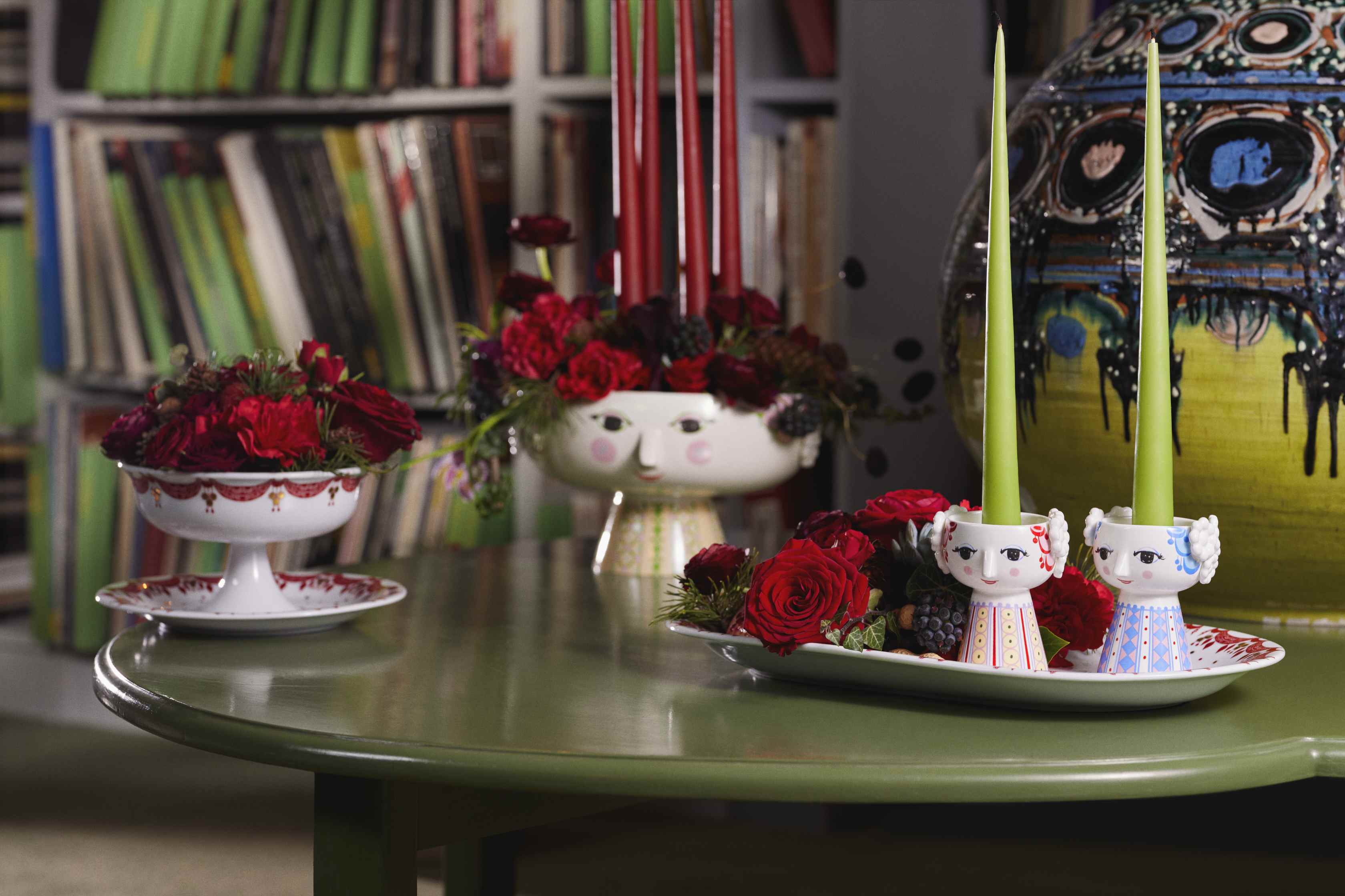 Dekorative Kerzenständer mit Gesicht und Blumenarrangements auf einem grünen Tisch, verspielte Wohnaccessoires.