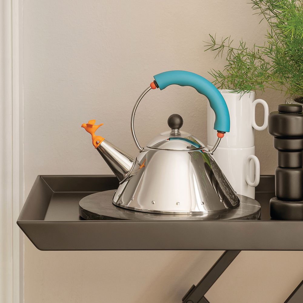 Alessi Wasserkessel 9093/1 LAZ aus Edelstahl mit blauem Griff und Vogelpfeife auf Tisch.