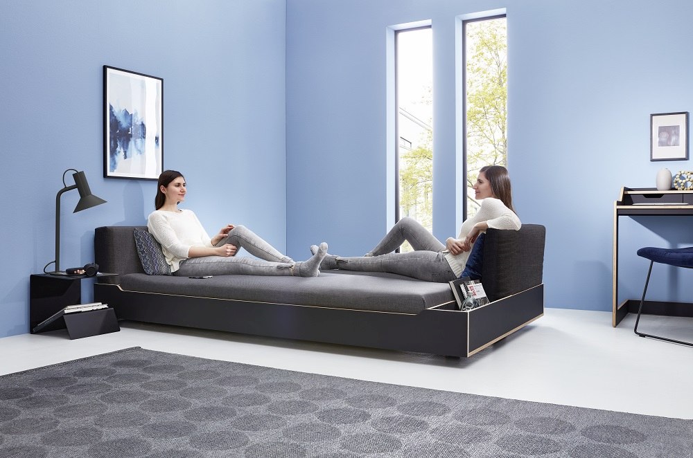 Maude Bett von Müller Möbelwerkstätten: Modernes Funktionsbett mit zwei Personen im hellen Raum.