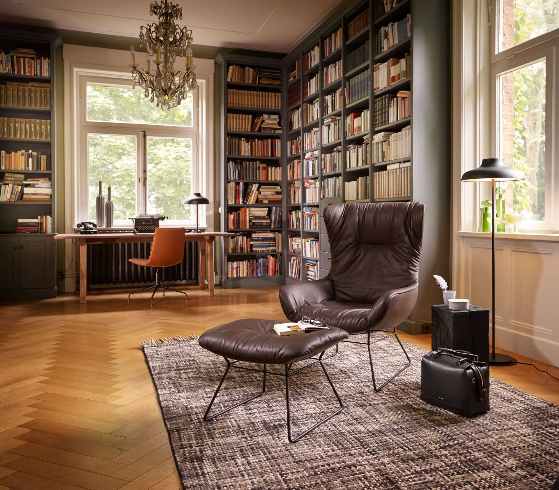 Leseecke mit braunem Ledersessel, Hocker, Bücherregal und Teppich. Gemütliches Wohnzimmer Interieur für entspanntes Lesen.