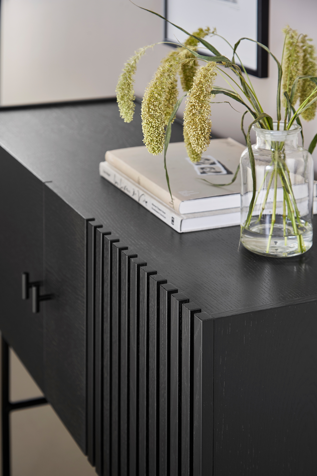 Detailaufnahme des schwarzen Array Sideboards von Woud (120cm) mit geriffelter Front, Büchern und Blumenvase.