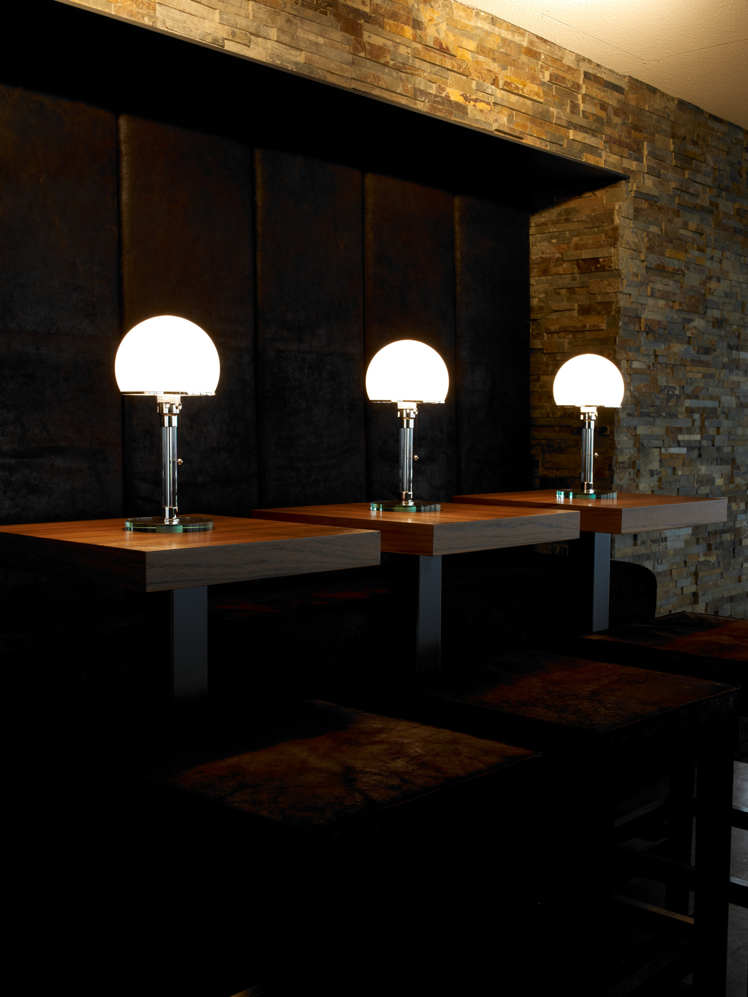 Drei WG24 Wagenfeld Tischleuchten von Tecnolumen auf dunklen Holztischen in einem eleganten Interieur.