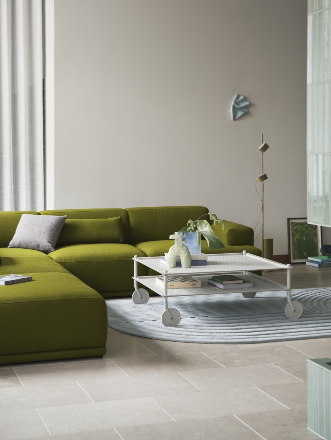 Muuto Flow Couchtisch auf Rollen, weiß, mit Pflanzen und Büchern dekoriert, vor grünem Sofa.