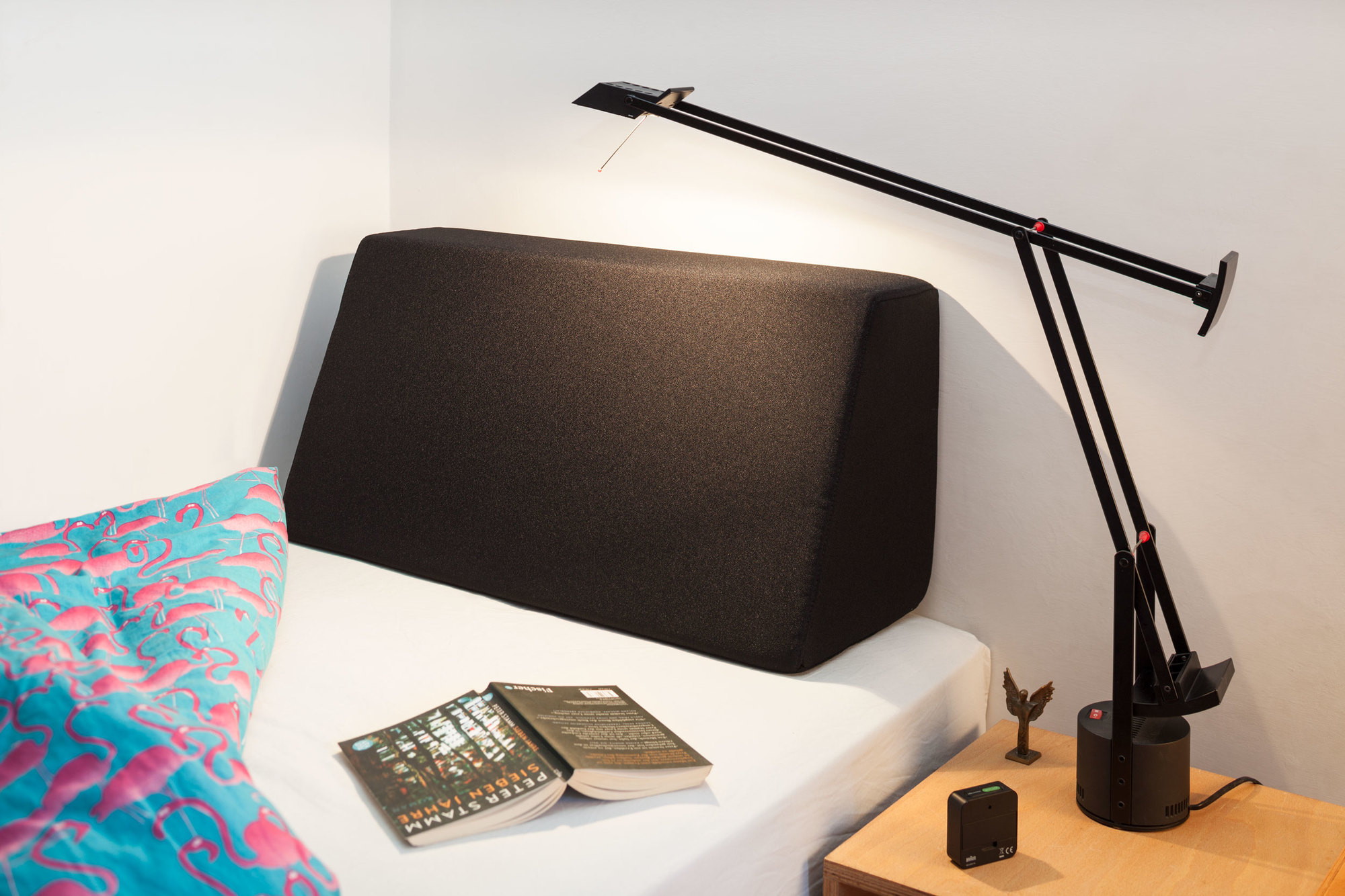 Schwarzes Tojo Lehn Rückenkissen auf einem Bett mit Lampe und Büchern. Bequemes Rückenkissen zum Anlehnen.