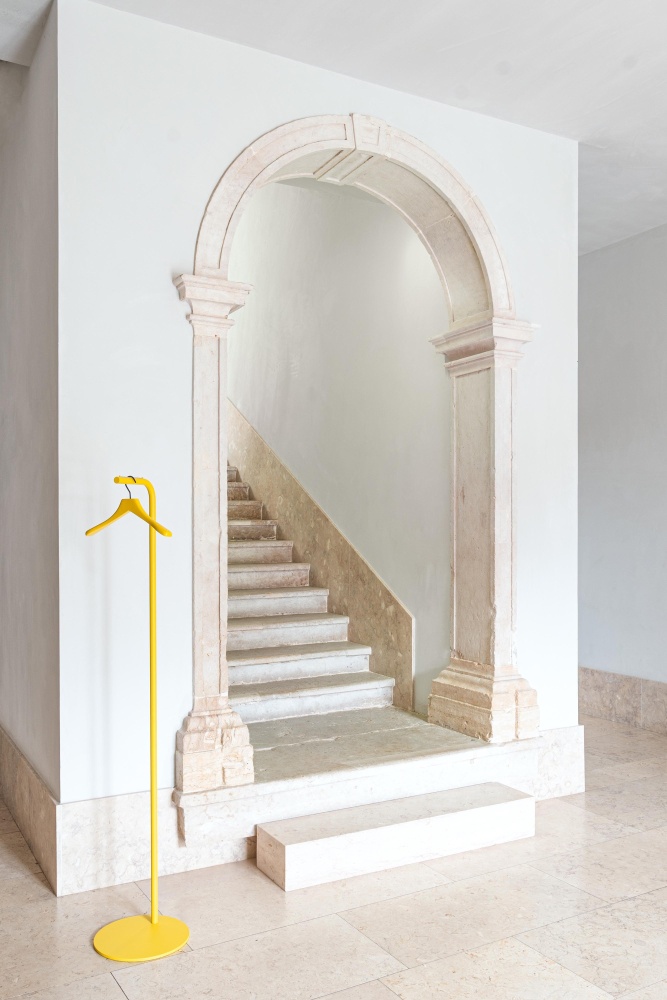 Gelber Bow Garderobenständer von Schönbuch im minimalistischen Flur mit Steintreppe und Bogen, moderne Flurmöbel.
