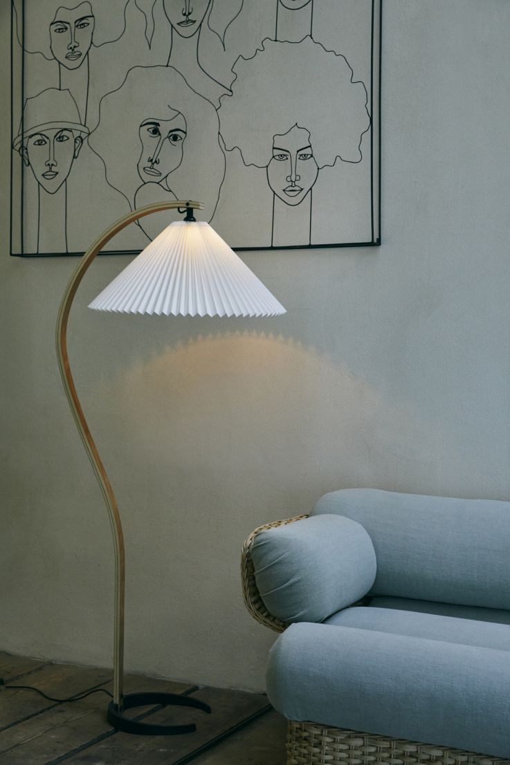 Elegante Timberline Stehlampe von Gubi mit plissiertem Schirm neben einem hellblauen Sofa und Wandbild.