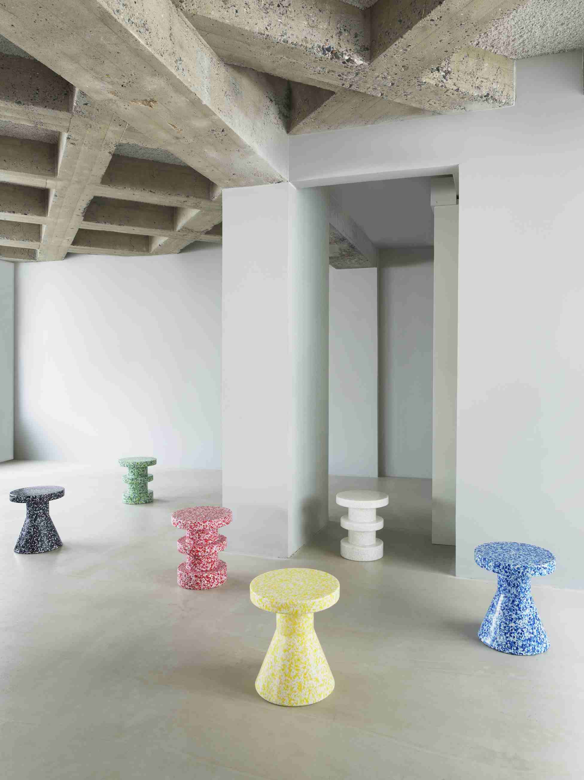 Mehrere farbenfrohe Bit Stool Hocker von Normann Copenhagen in einem minimalistischen Raum mit Betonstruktur.