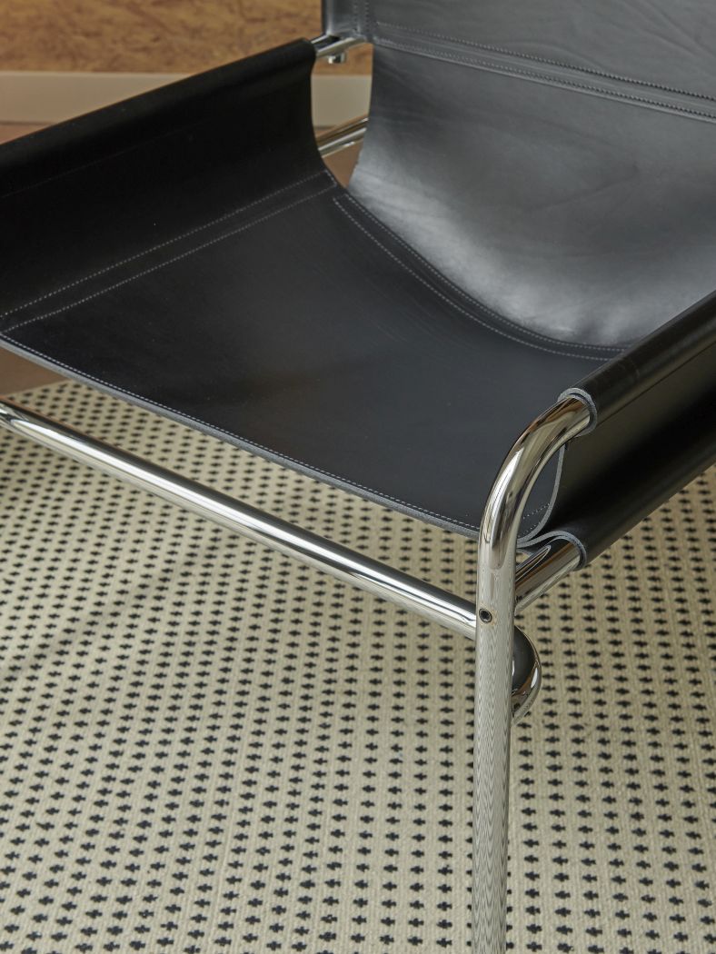 Detailaufnahme des SZ 14 Sessel Spectrum mit schwarzem Leder und verchromtem Stahlrohrgestell auf gemustertem Teppich.