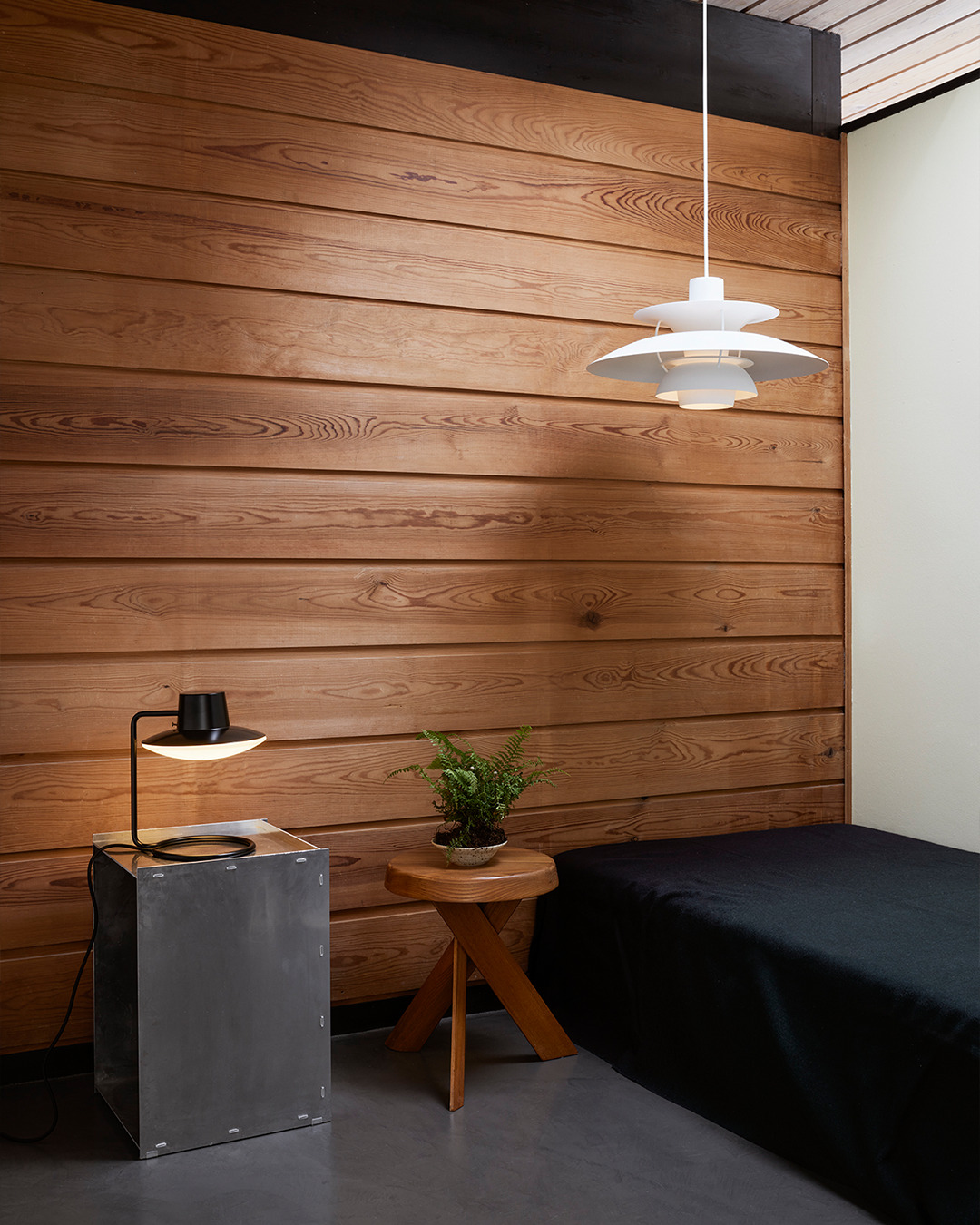 Innenaufnahme mit weißer Pendelleuchte, schwarzer Tischleuchte und Holzwand. Moderne Lampen für Wohnzimmer und Schlafzimmer.