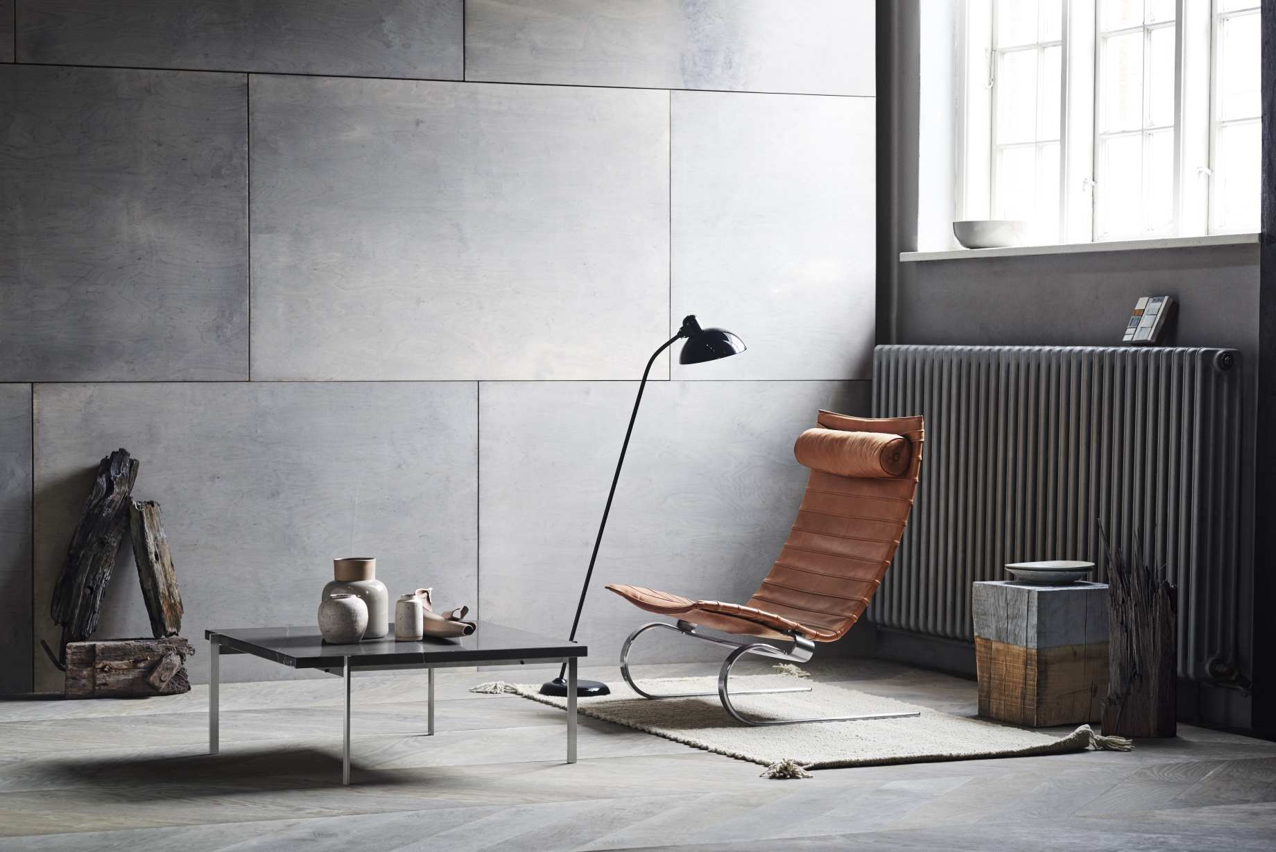 Interieur mit PK 61 Couchtisch von Fritz Hansen, Design-Lampe und Ledersessel auf einem Teppich.