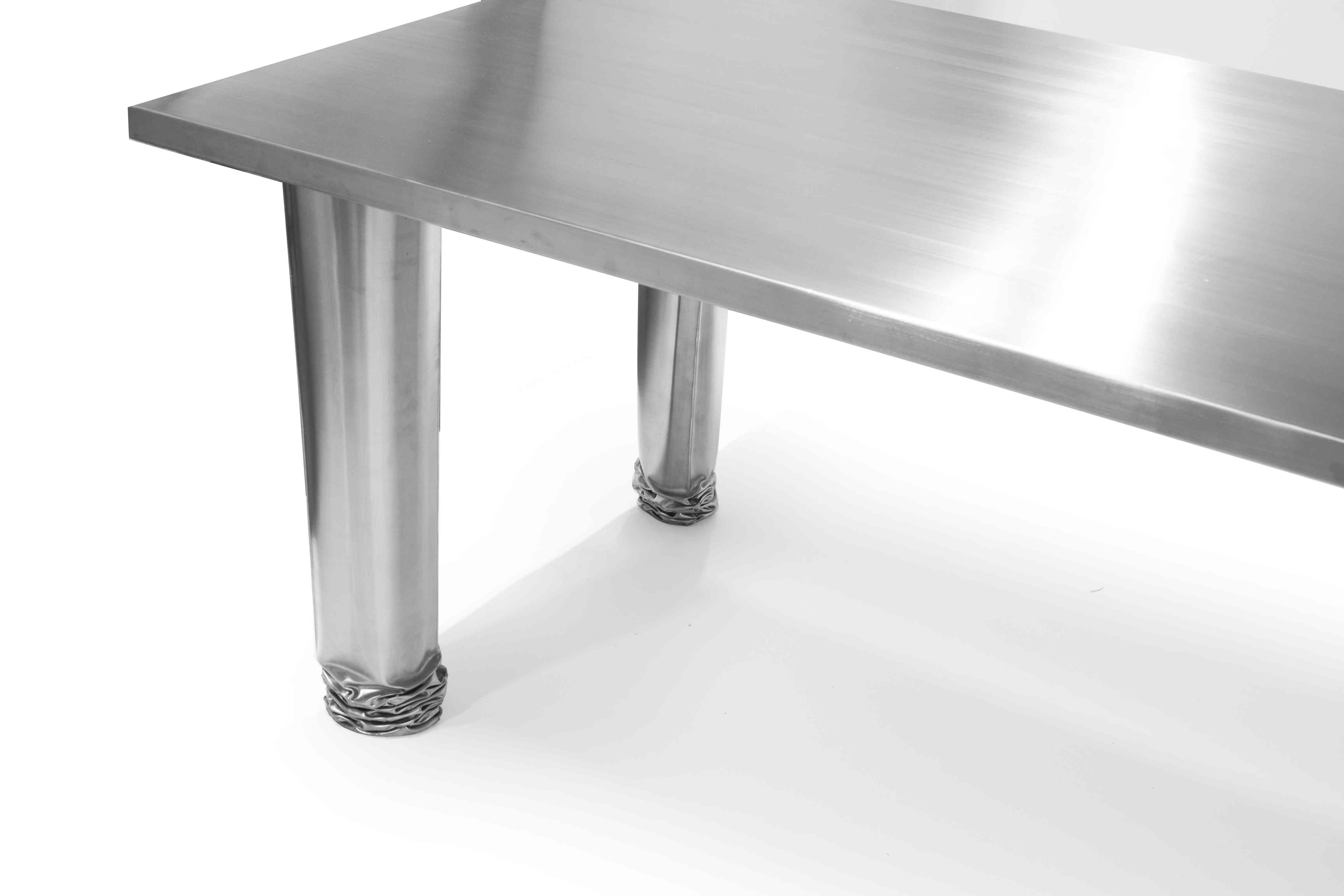 Detailaufnahme des Zieta Crash Table Esstisches aus poliertem Stahl mit einzigartigen, verformten Tischbeinen.