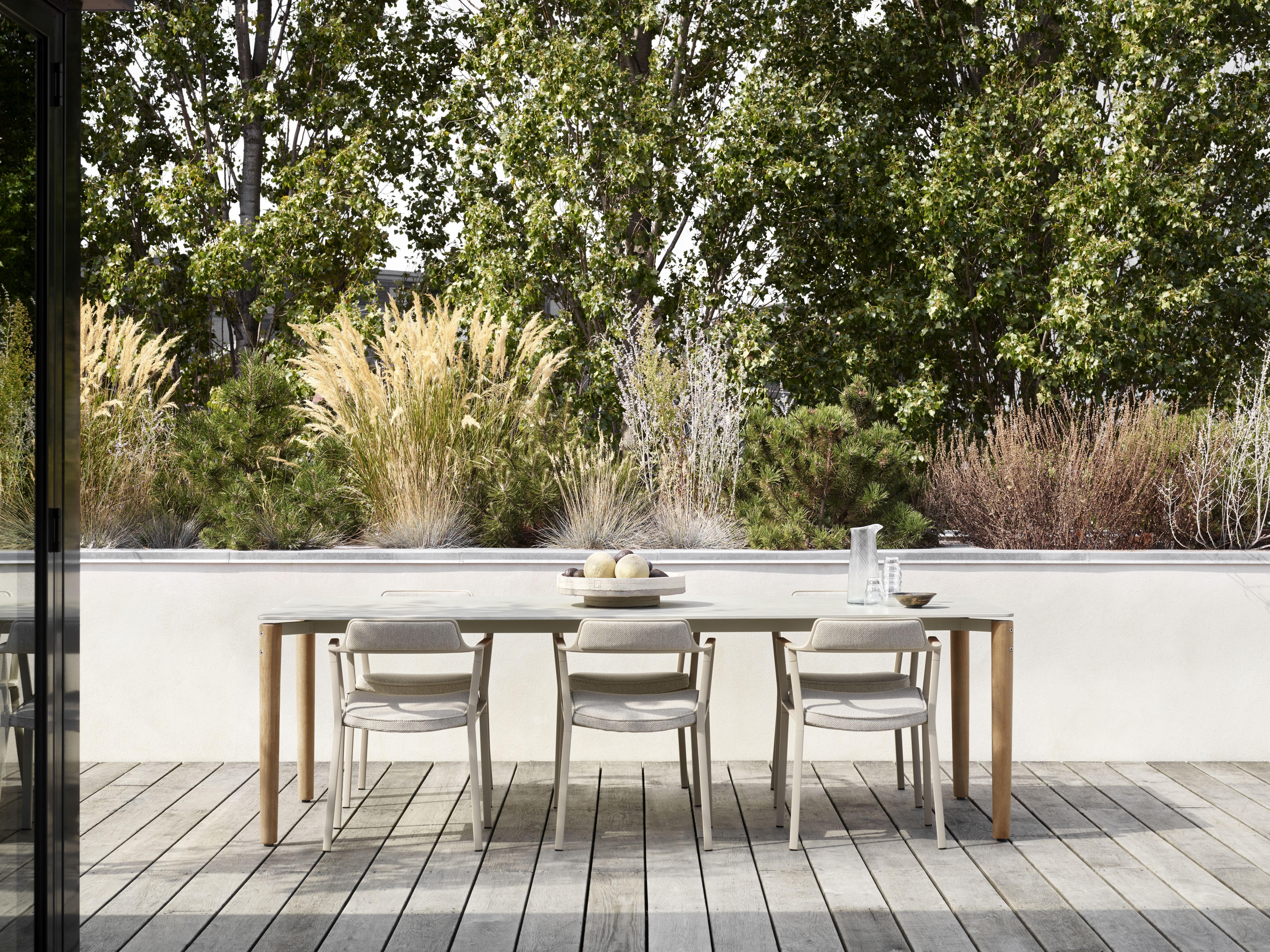 Vipp Open-Air Outdoor Tisch mit Stühlen auf einer Holzterrasse vor üppigem Grün. Gartenmöbel.