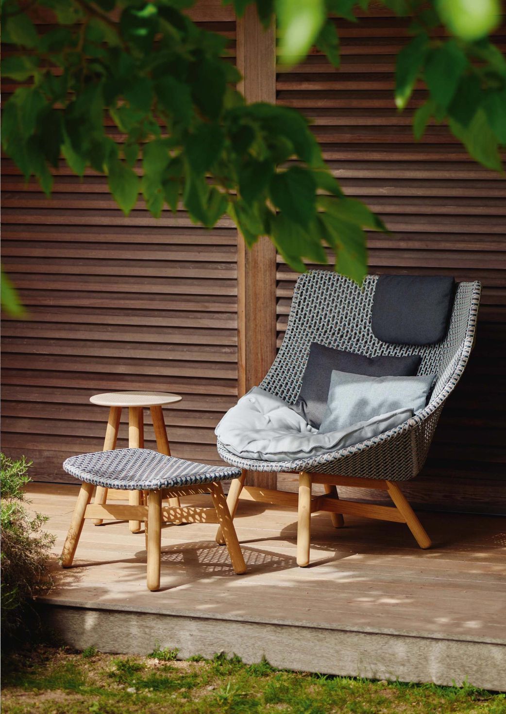Geflochtener Outdoor Sessel mit Fußhocker und Beistelltisch für Garten oder Terrasse. Bequeme Gartenmöbel mit Kissen.