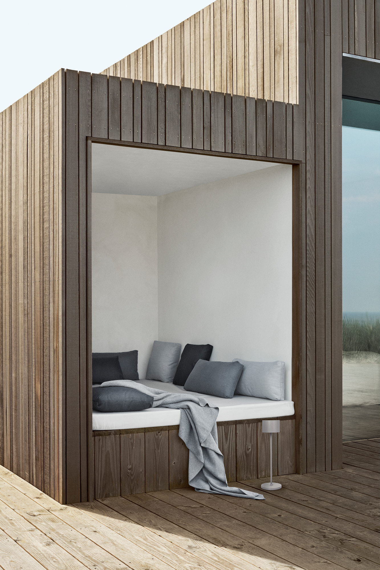 Gemütliche Sitzecke im Freien mit grauen STAY Kissen von Blomus und weicher Decke.