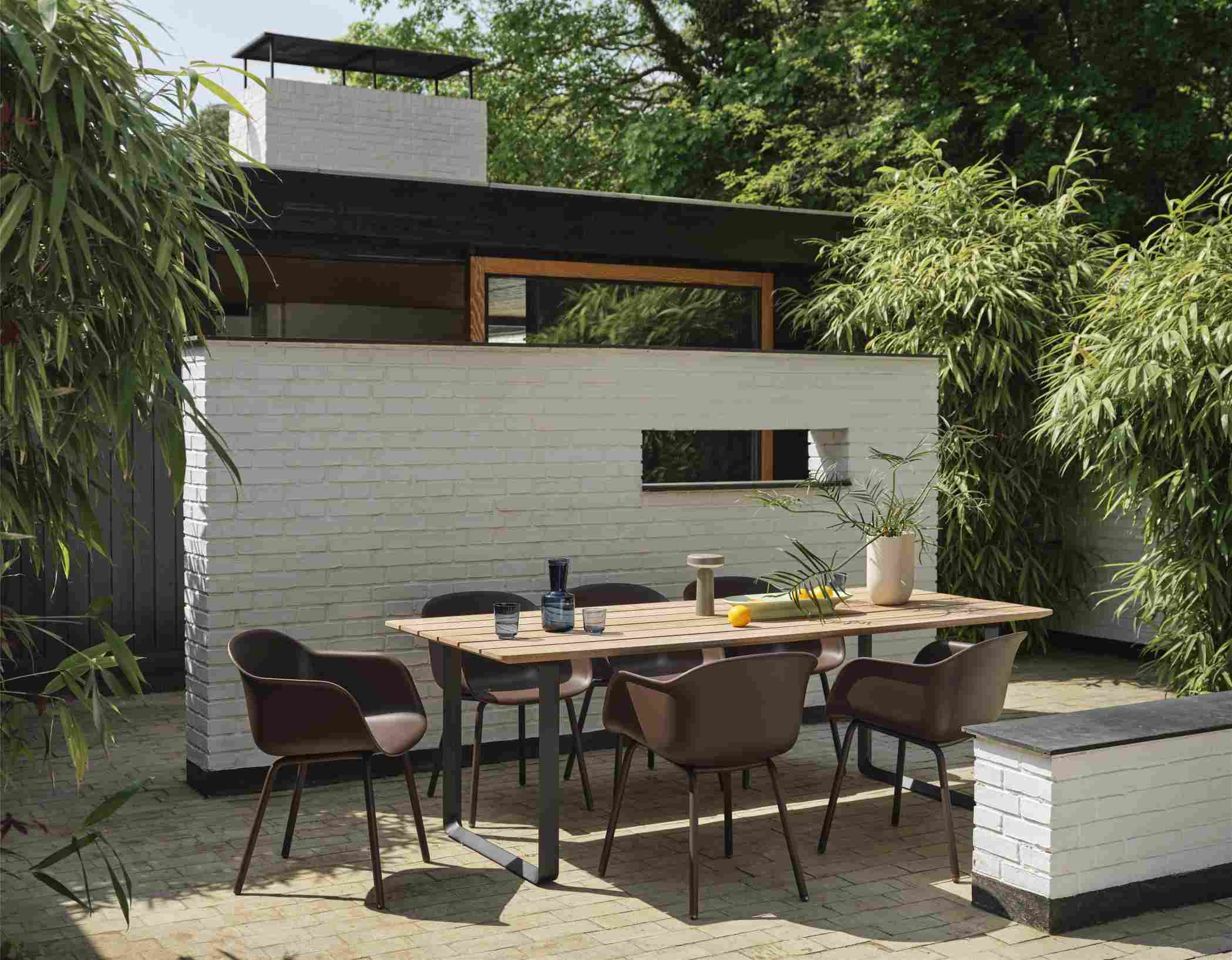 Muuto Kink Vase Sand auf einem Gartentisch mit Stühlen und Pflanzen im Hintergrund.