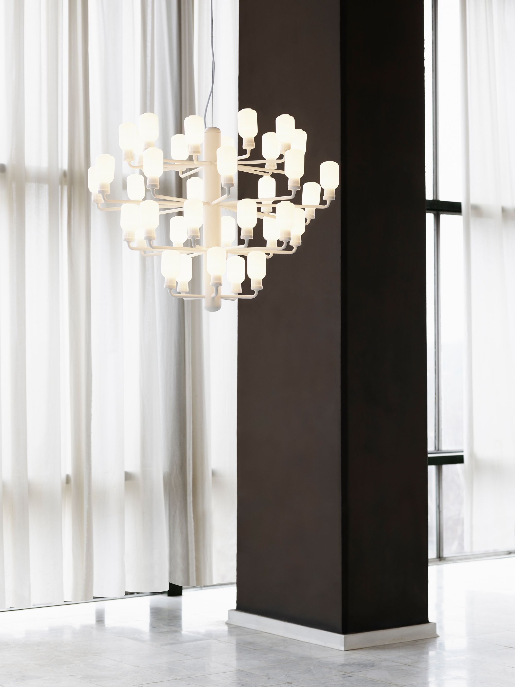 Weiße Amp Chandelier Pendelleuchte von Normann Copenhagen im modernen Interieur mit Vorhängen und Marmorboden.