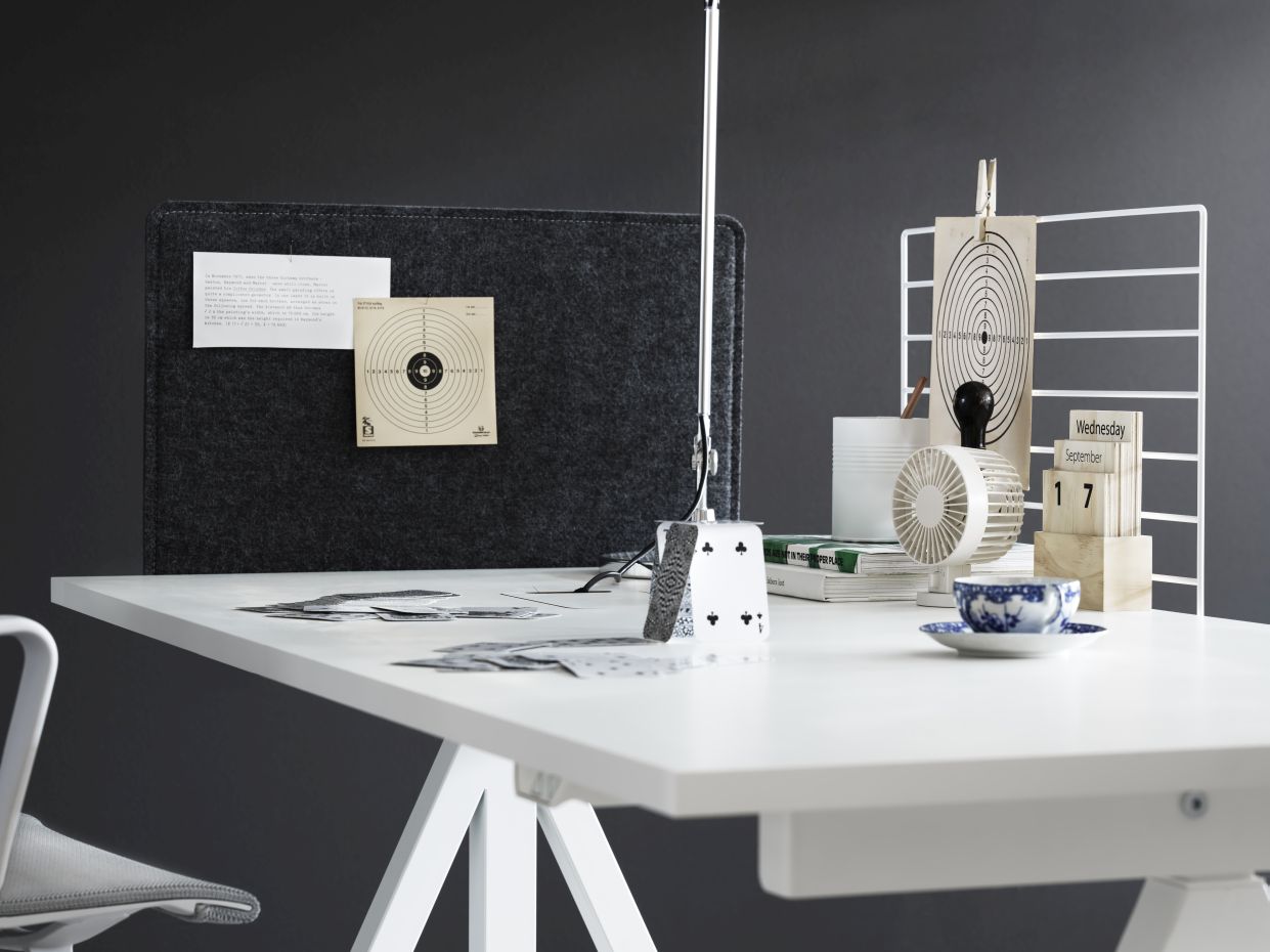 Detailaufnahme eines weißen Schreibtischs von String Furniture, höhenverstellbar, mit diversen Büroaccessoires dekoriert.
