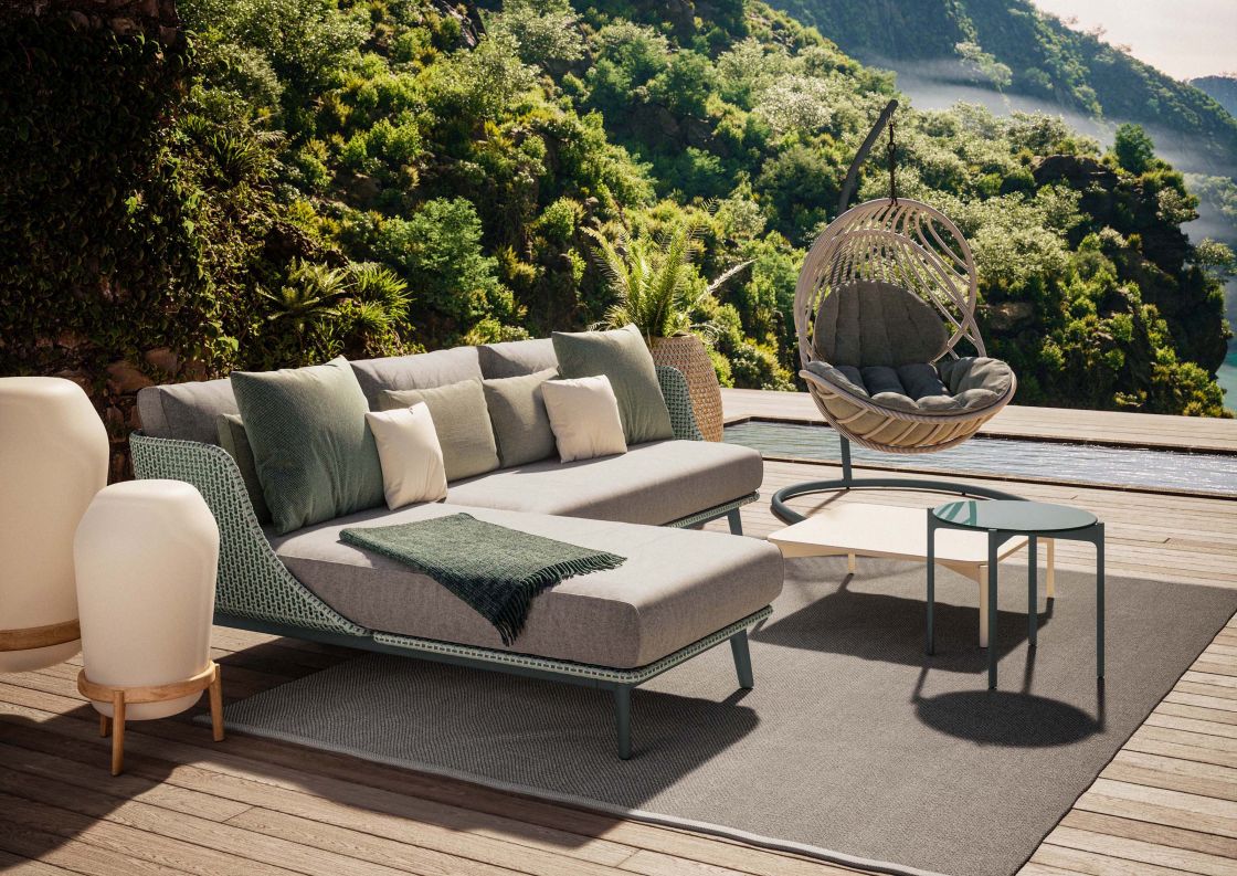 Mbarq 3-Sitzer Outdoor Sofa von Dedon mit Polstern und Gartenmöbeln auf einer Terrasse.