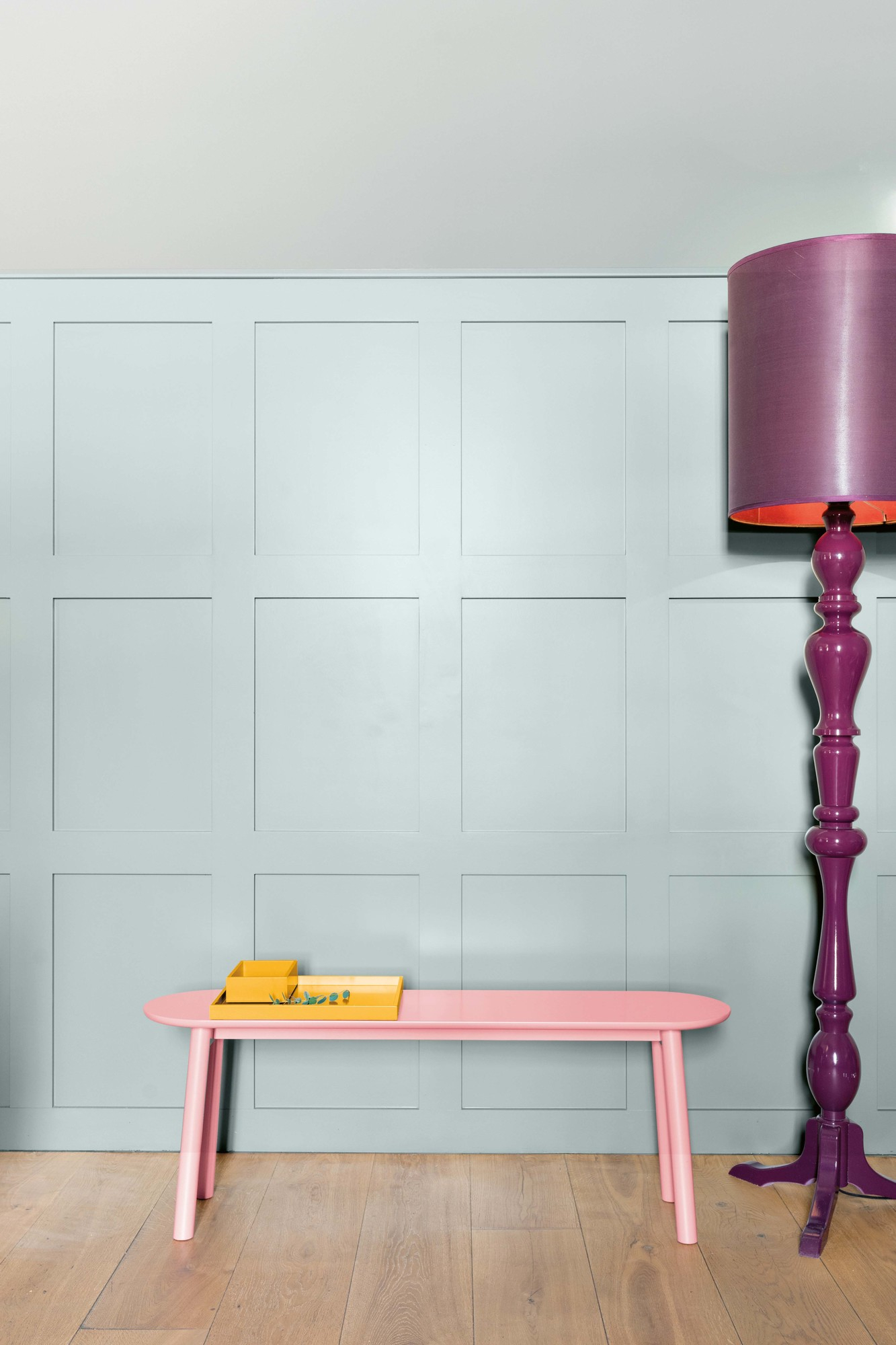 Mala Sitzbank von Schönbuch, rosa Bank mit Ablage und lila Stehlampe vor hellblauer Wand.