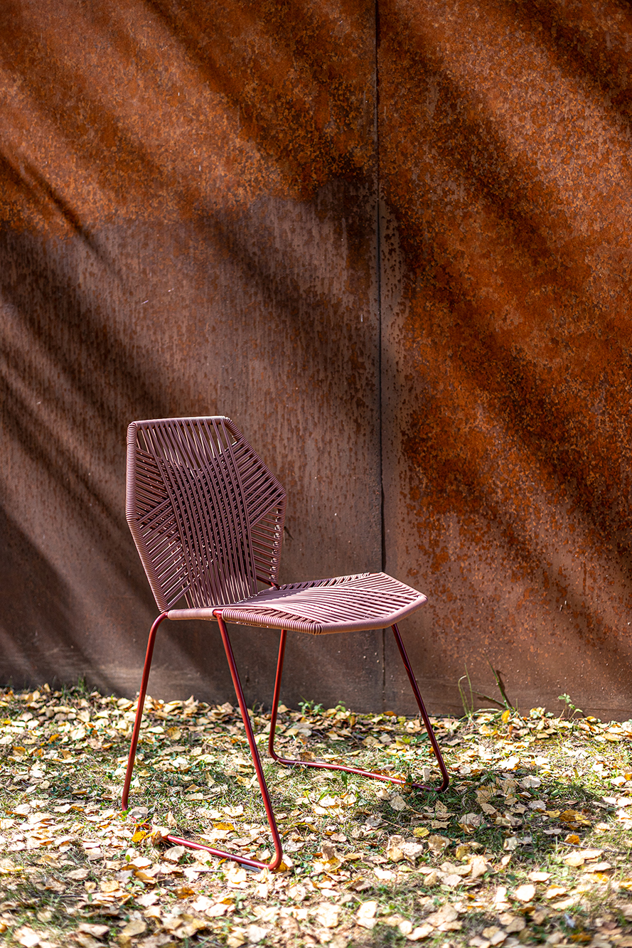 Tropicalia Outdoor Stuhl von Moroso, rosafarbenes Polymergeflecht, vor einer rostfarbenen Wand auf Rasen mit Blättern.
