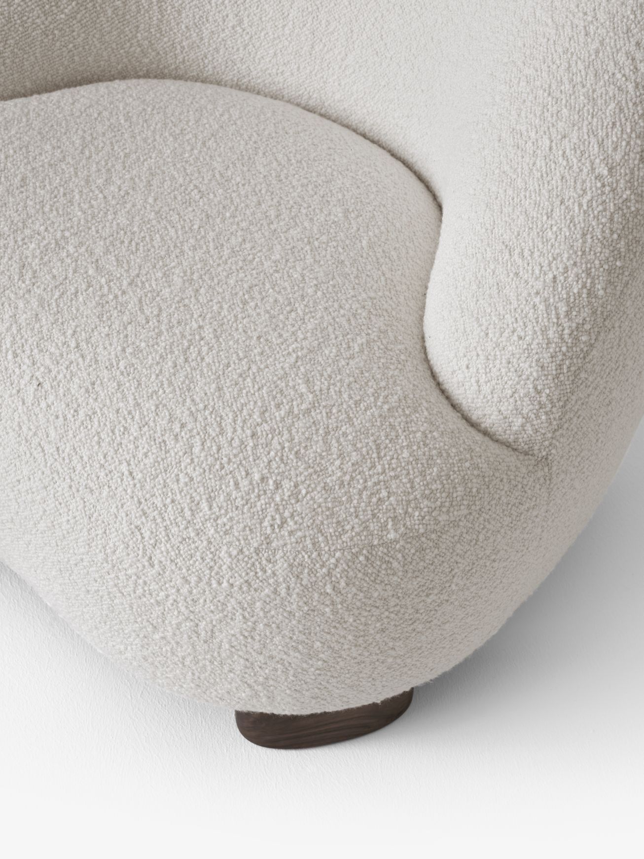 Detailaufnahme des Margas Loungesessels LC1 von AndTradition mit cremefarbenem Bouclé-Bezug und dunklem Holzfuß.