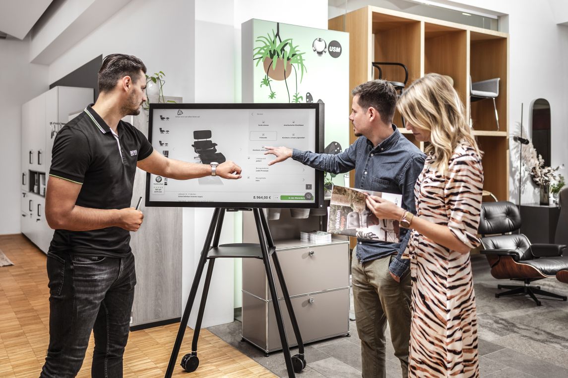 Kunden betrachten USM Möbelkonfigurator auf Display: Design Büromöbel, Regalsysteme und Konferenztische.