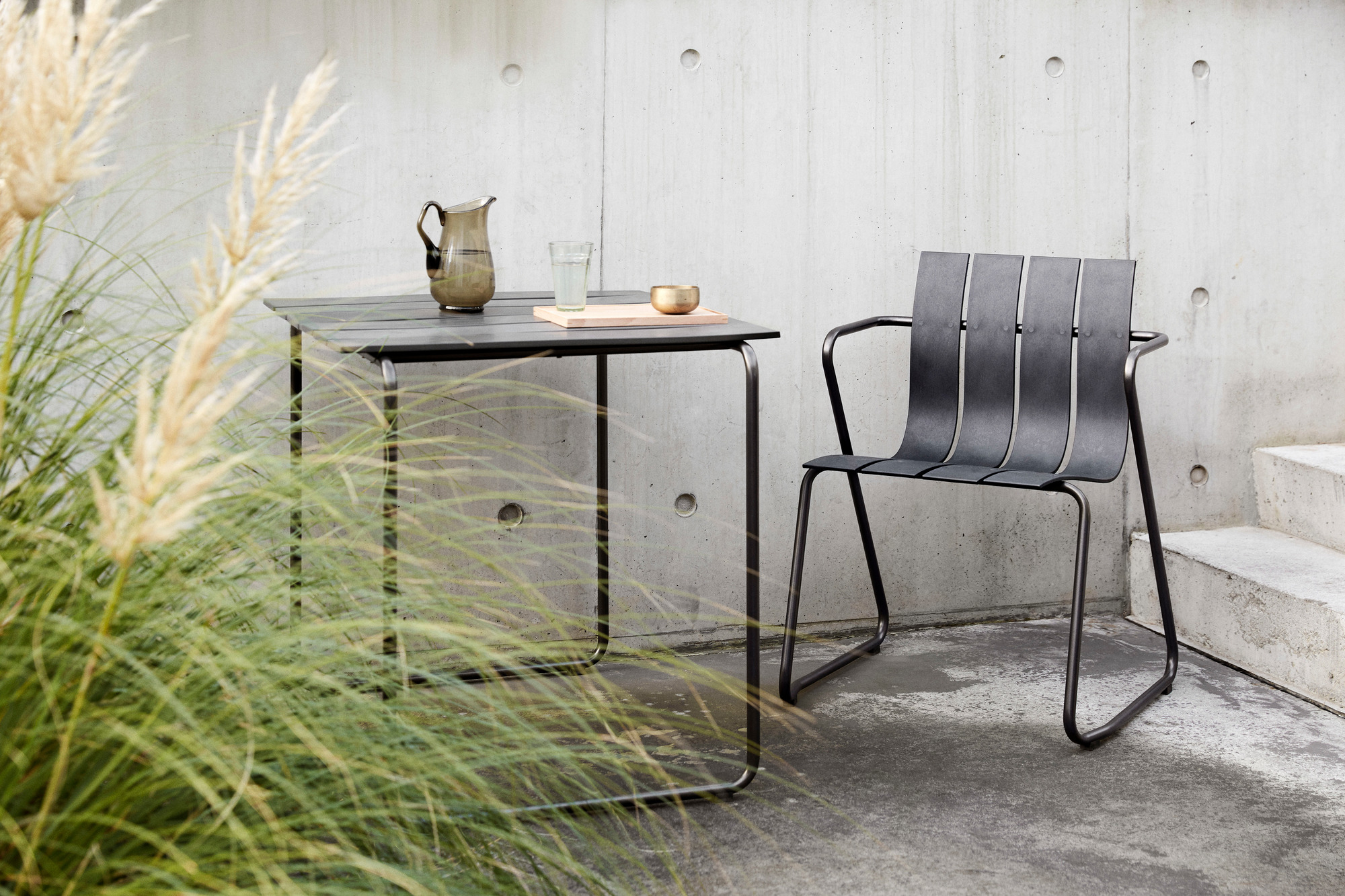 Ocean Chair von Mater, ein schwarzer Outdoor Stuhl aus recyceltem Kunststoff neben einem Gartentisch.