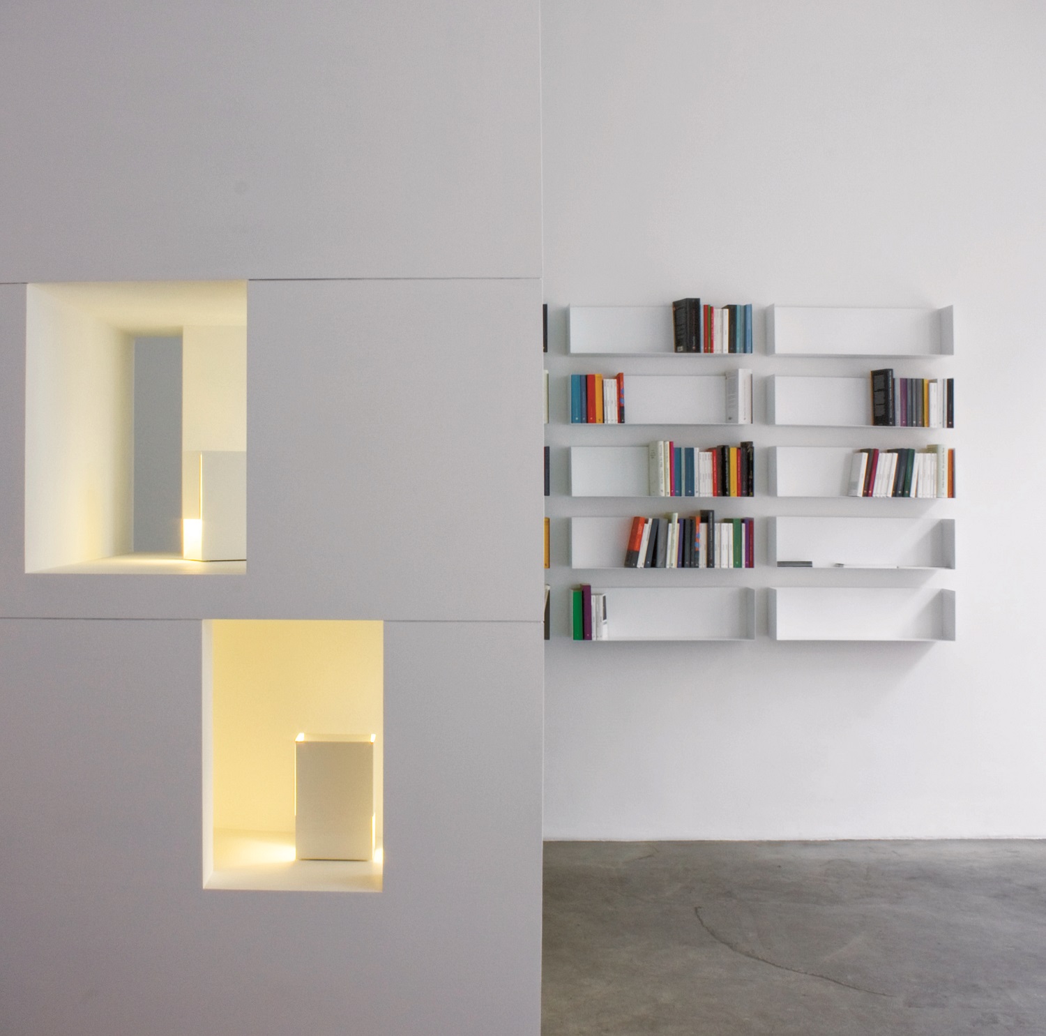 Helles, minimalistisches Bücherregal von Müller Möbelwerkstätten, weiße Regale mit Büchern an einer weißen Wand.