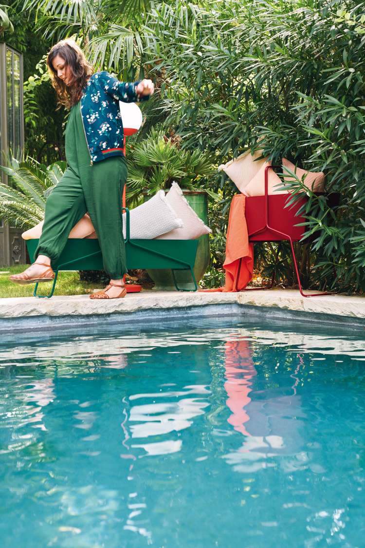 Hochwertiger Fermob Basket Blumenkasten in Grün und Rot neben einem Pool, mit Kissen.