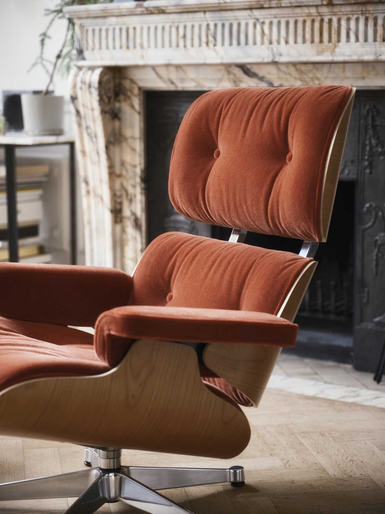 Nahaufnahme eines Eames Lounge Chair Sessels in orange mit Holzrahmen und Knopfdetails vor Kamin.