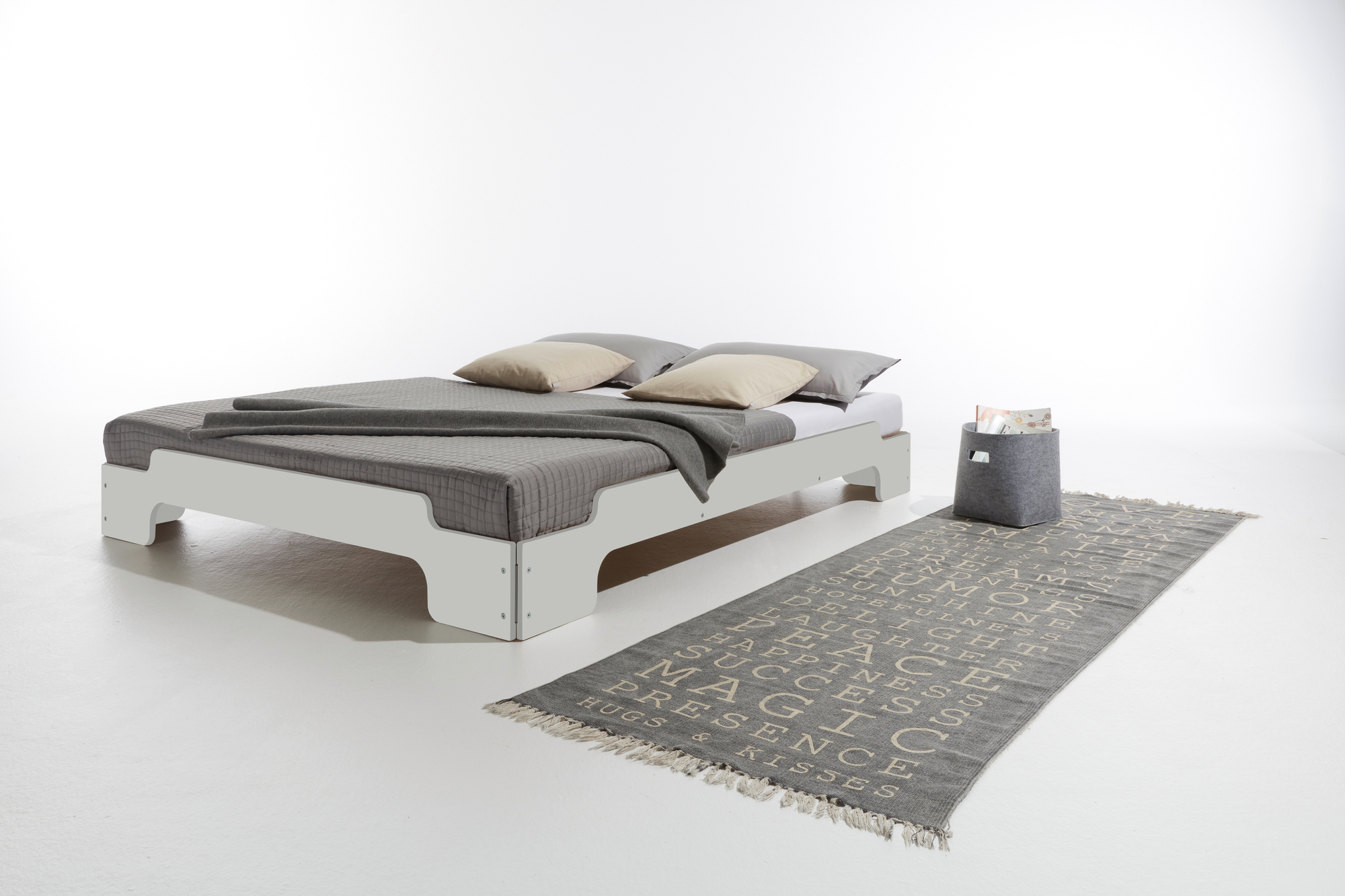 Weiße Stapelliege CPL von Müller Möbelwerkstätten mit grauer Tagesdecke, Kissen und Teppich im Schlafzimmer.