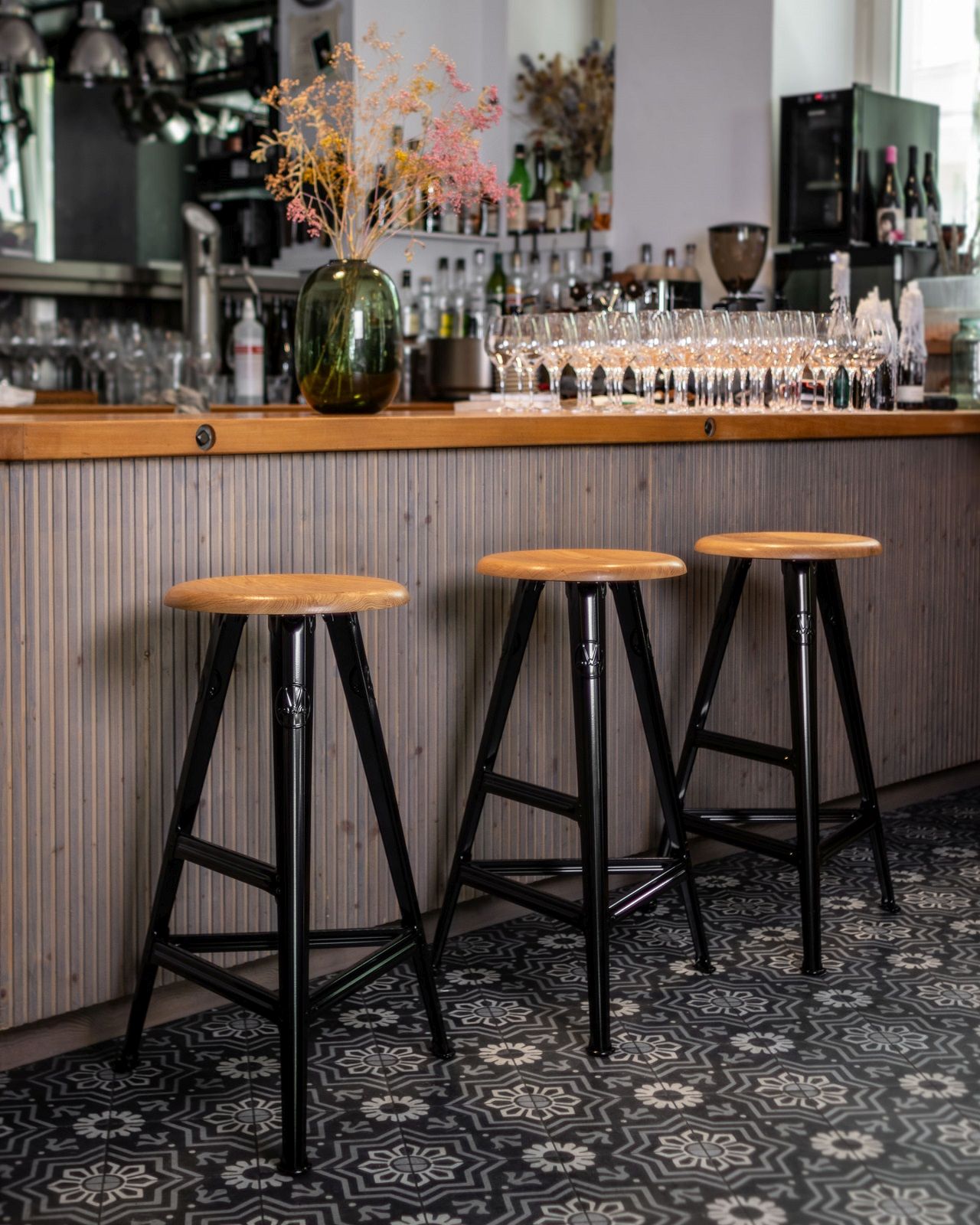 Drei Rowac Barhocker Modell I 75 cm aus Holz und Stahl vor einer Bar.