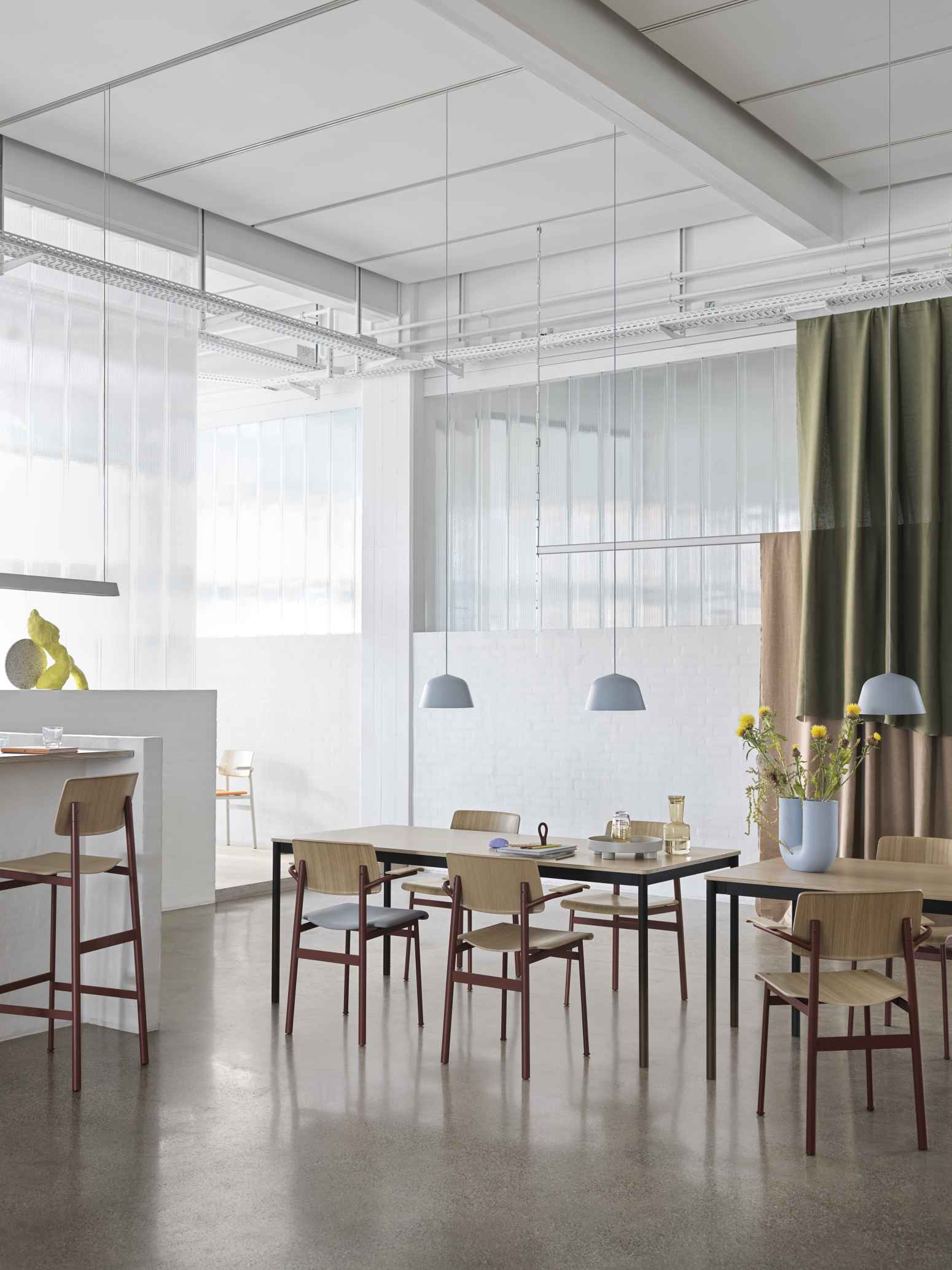 Heller Raum mit Esstisch und Muuto Loft Chair Stühlen aus Holz und farbigem Metall.
