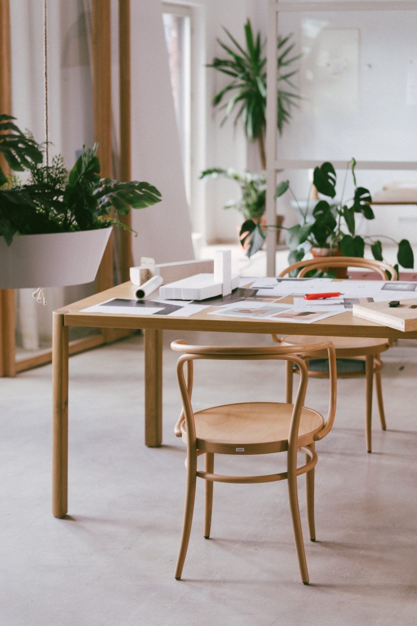 Heller Thonet 1140 Esstisch aus Holz mit Stühlen, Pflanzen und Arbeitsmaterialien in einem hellen Raum.