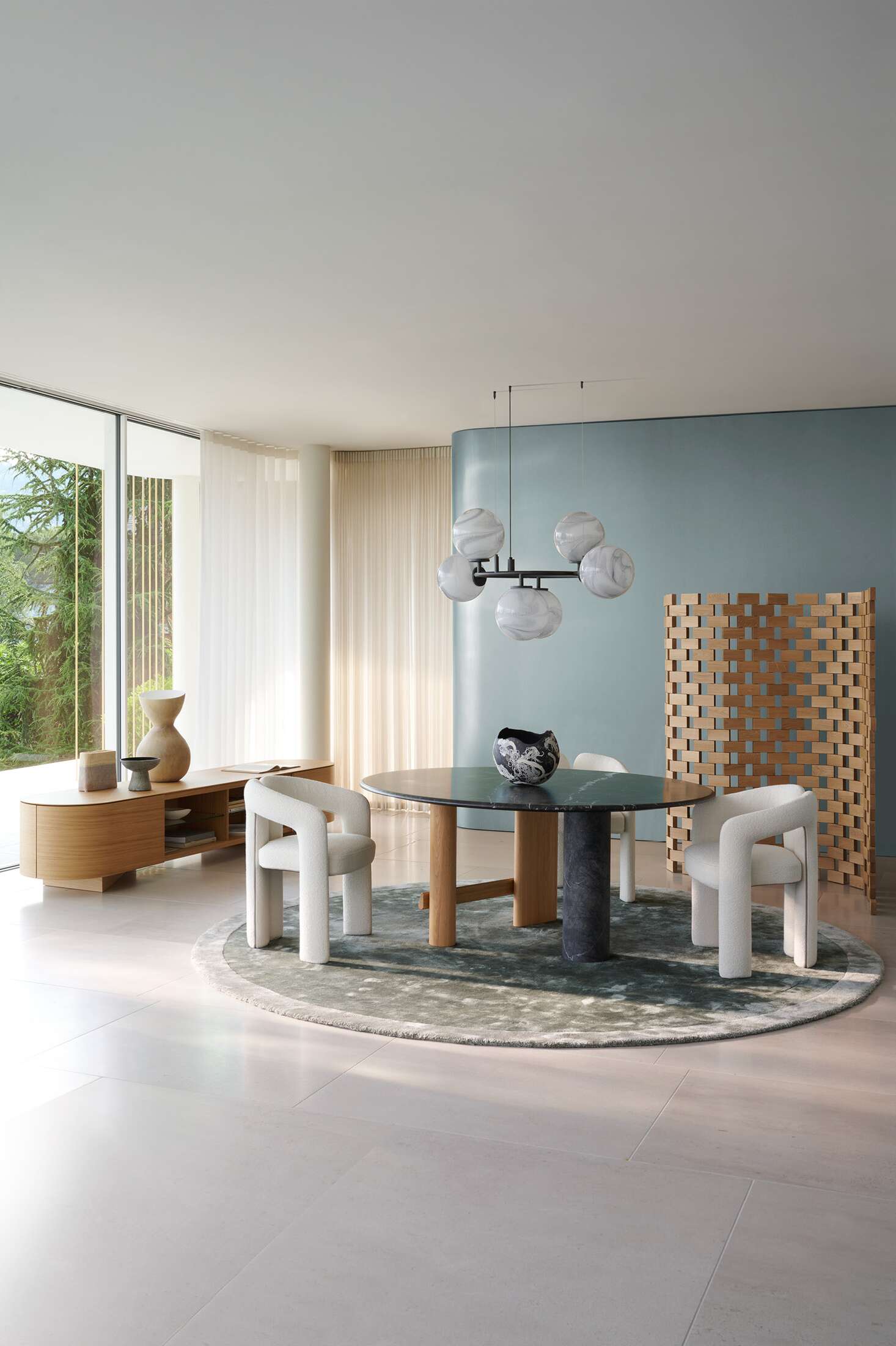 Innenaufnahme eines Esszimmers mit Cassina Dudet Sessel in Weiß, rundem Tisch und moderner Beleuchtung.