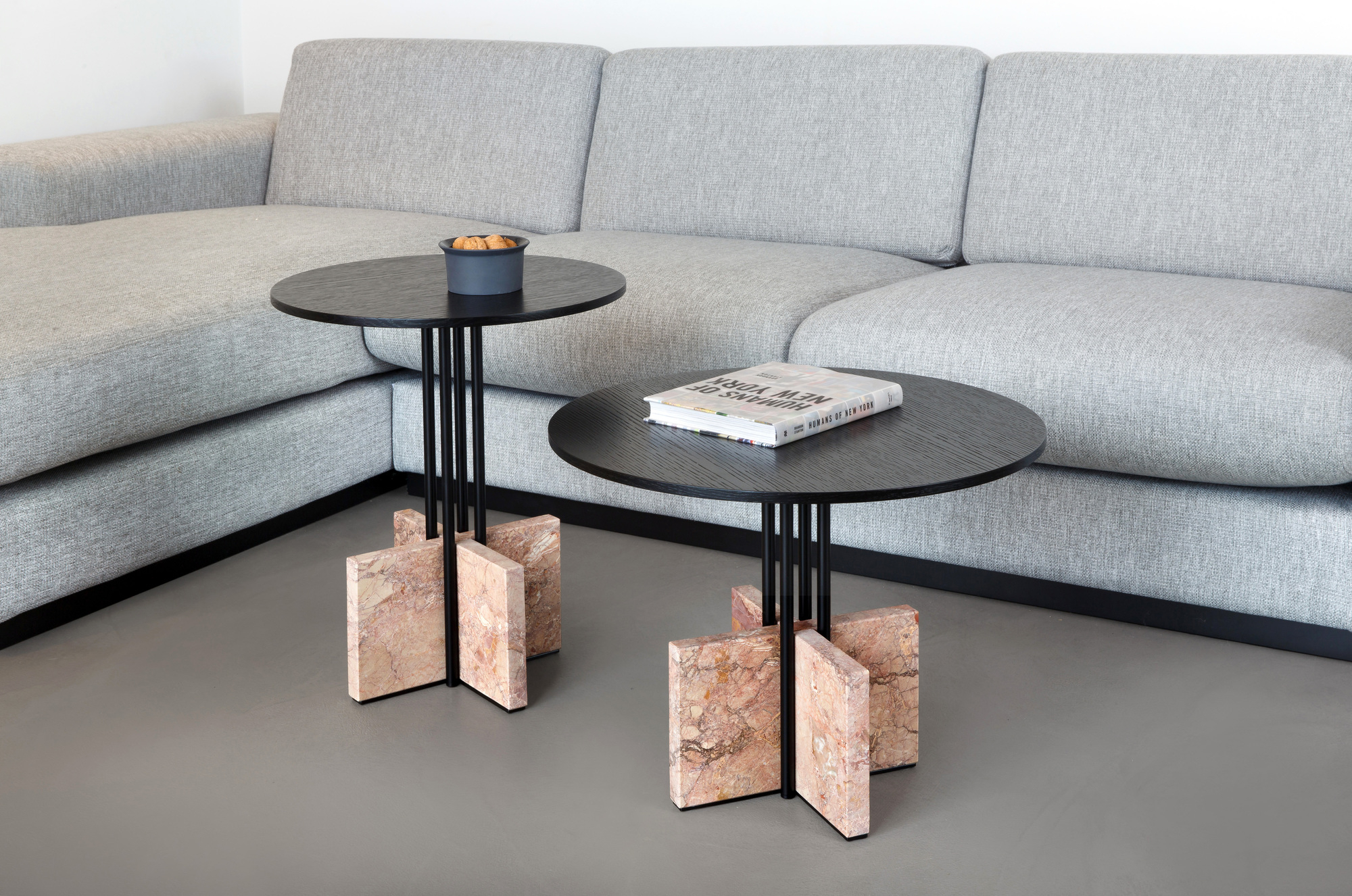 Zwei Gravity Table Beistelltische Favius mit schwarzer Tischplatte und Marmorfuß neben einem grauen Sofa.